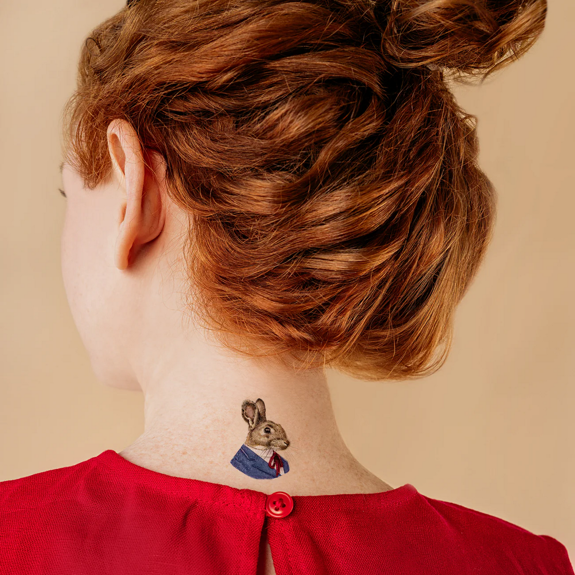 Person with a rabbit tattoo on their neck against a beige background