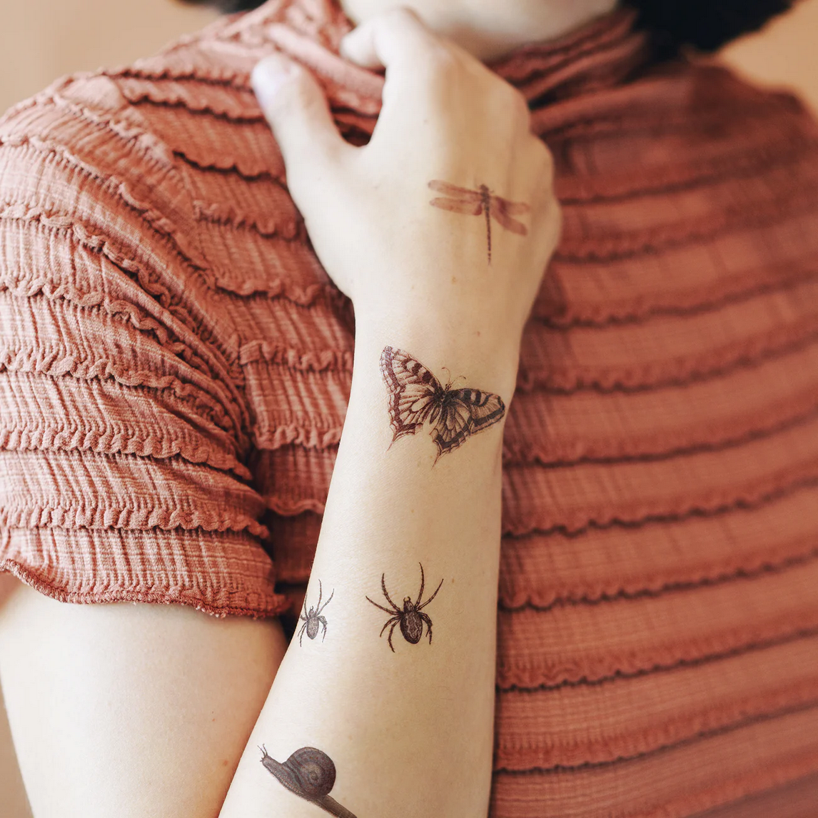 Person wearing temporary tattoos of a butterfly, spider, and snail on their arm.