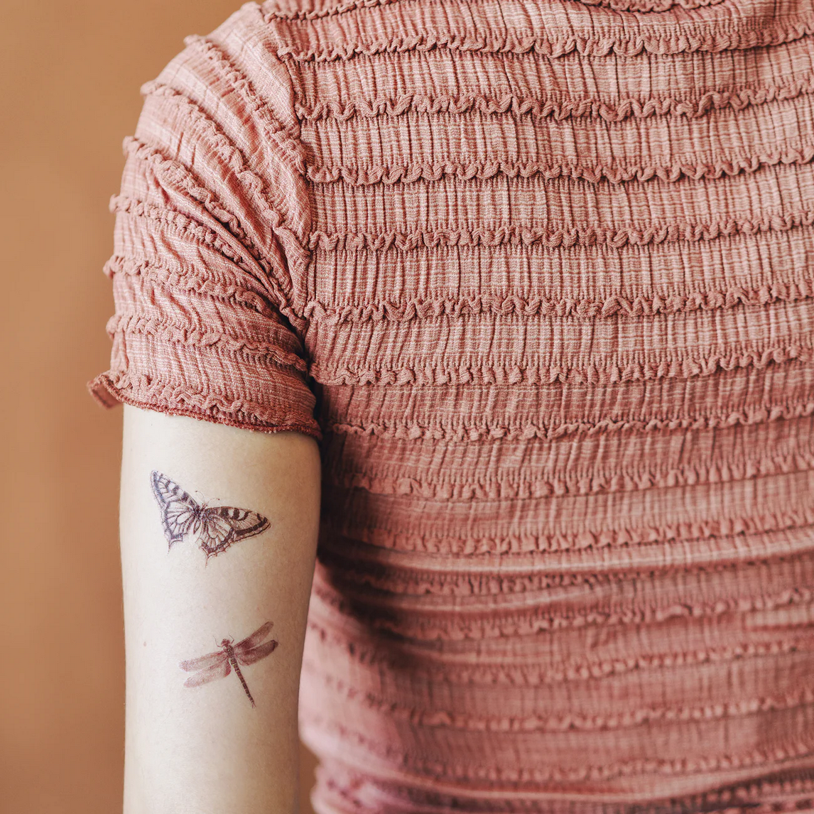 Person wearing a textured pink dress with tattoos on their arm against a beige background