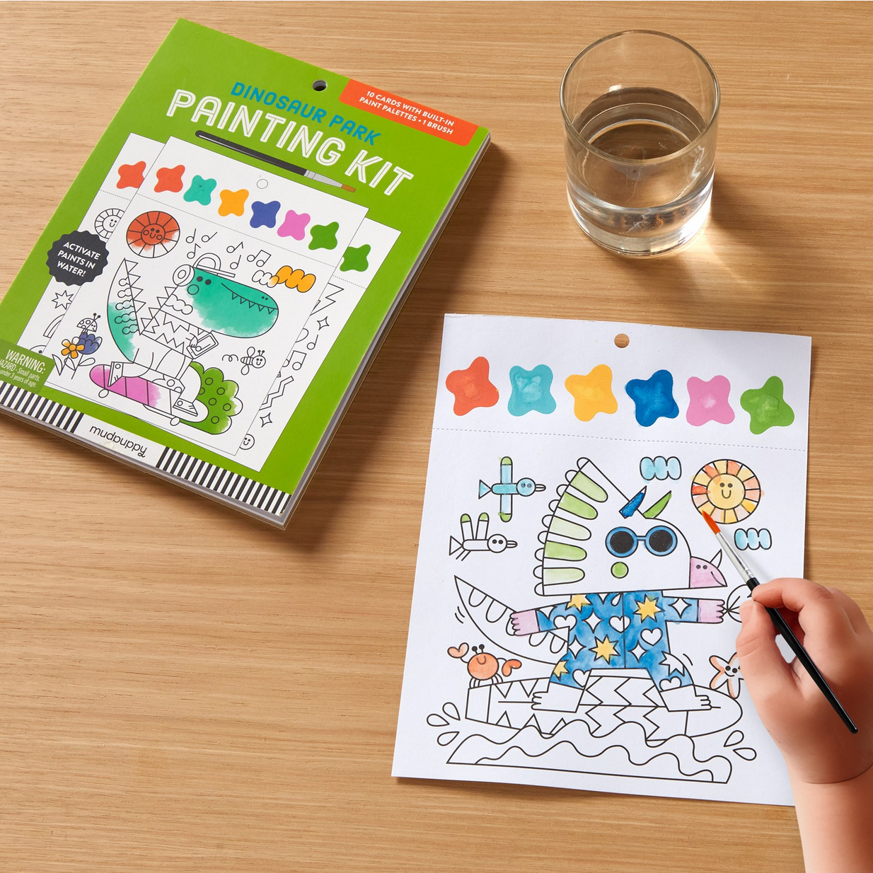 Dinosaur-themed painting kit with coloring sheet and water glass on a wooden surface