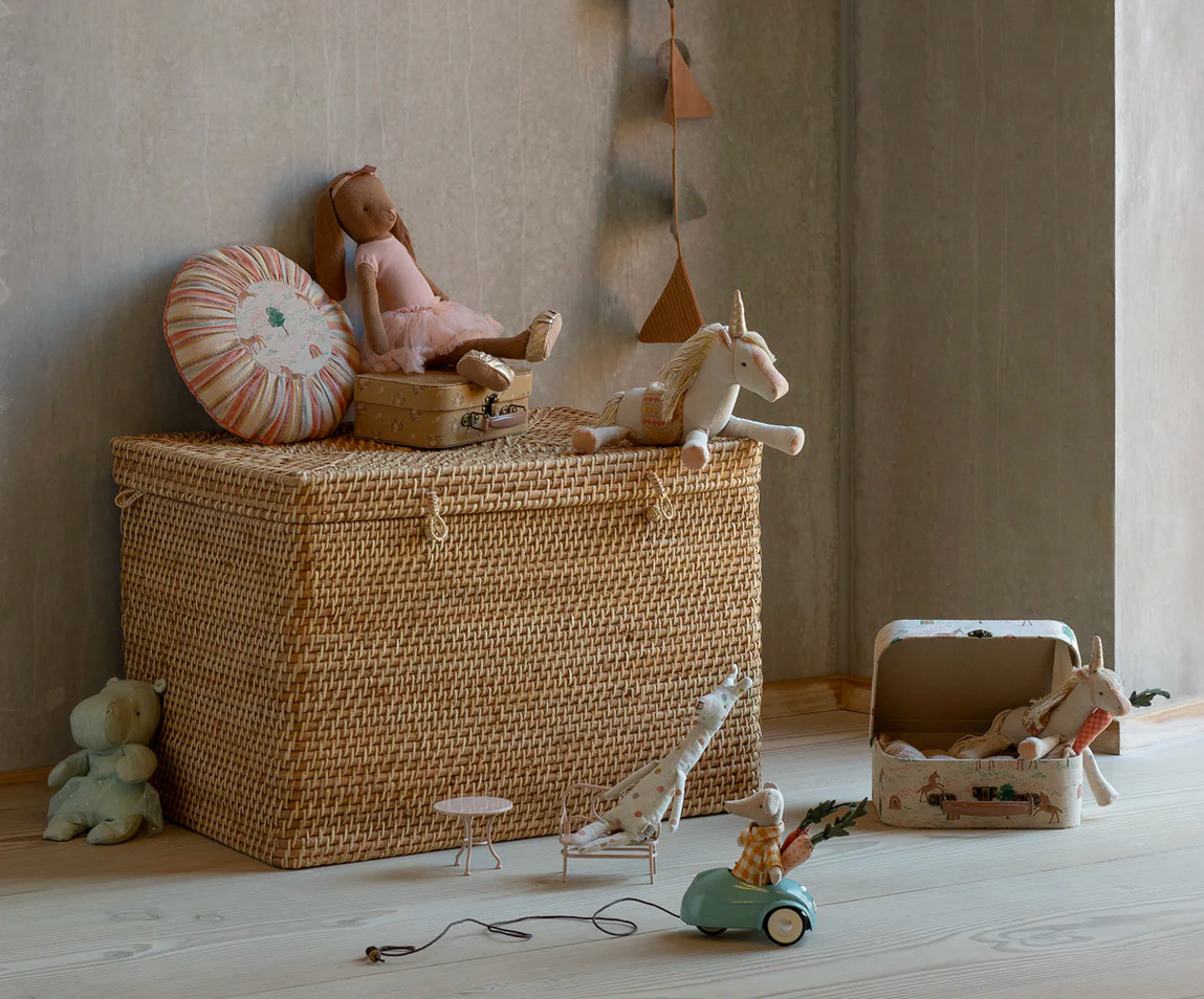 Wicker toy box with stuffed animals and toys on a wooden floor against a neutral wall.