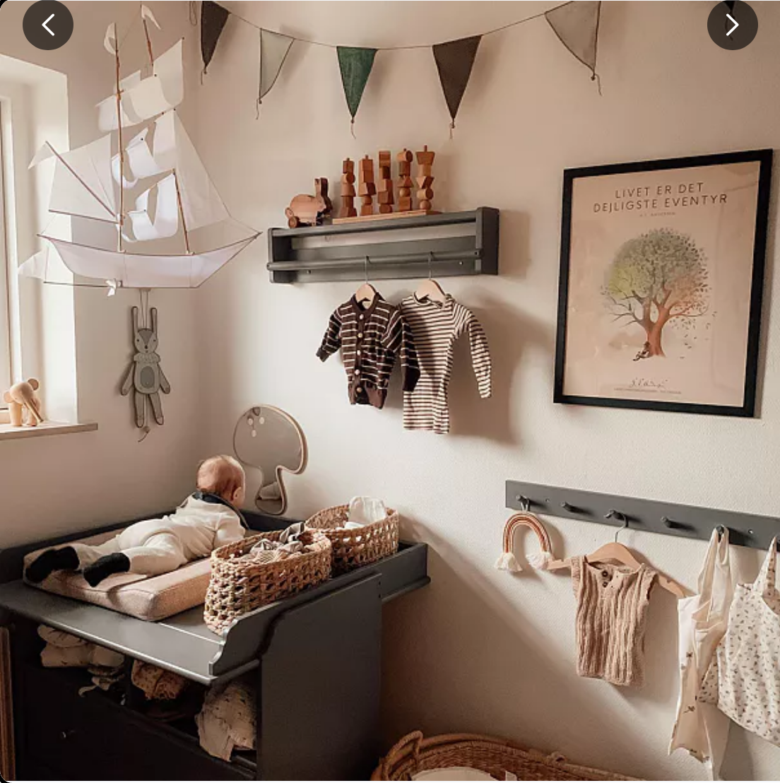 Children's room with baby lying on a changing table, clothes hanging, and wall decorations.