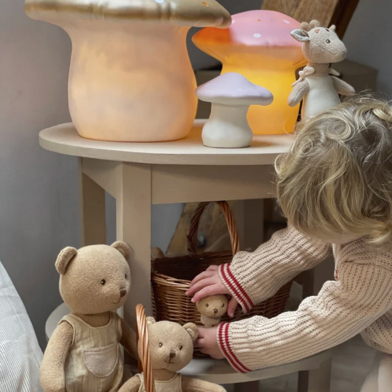 Child playing with teddy bears in a basket next to a small table with decorative lamps.