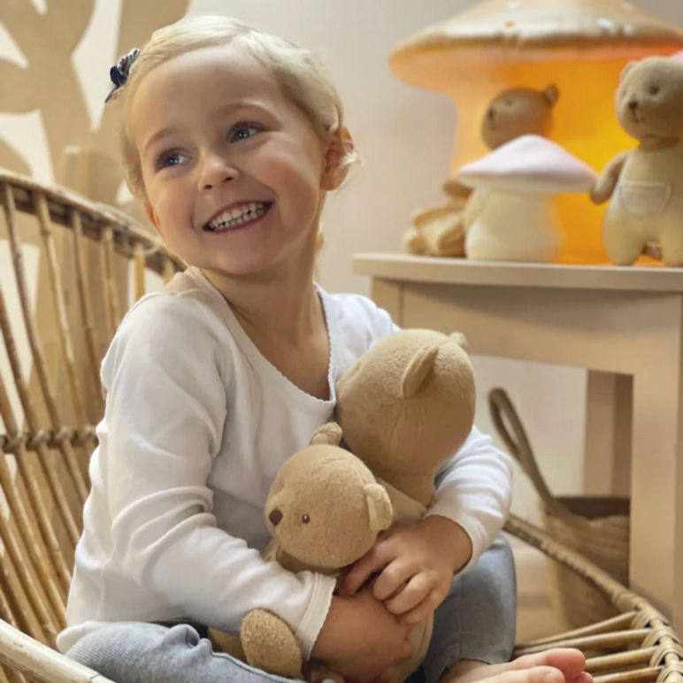 Child holding a teddy bear in a wicker chair with toys in the background