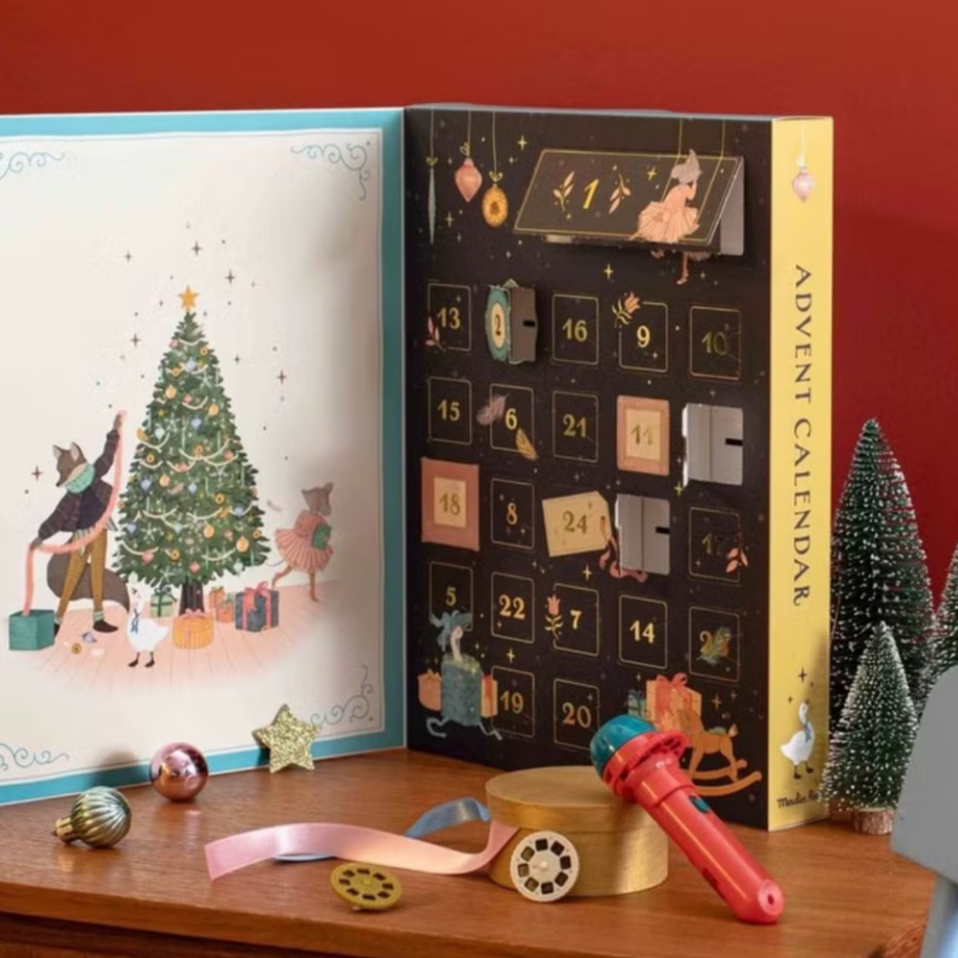 Advent calendar open to a Christmas-themed page with small trees and toys on a wooden surface.