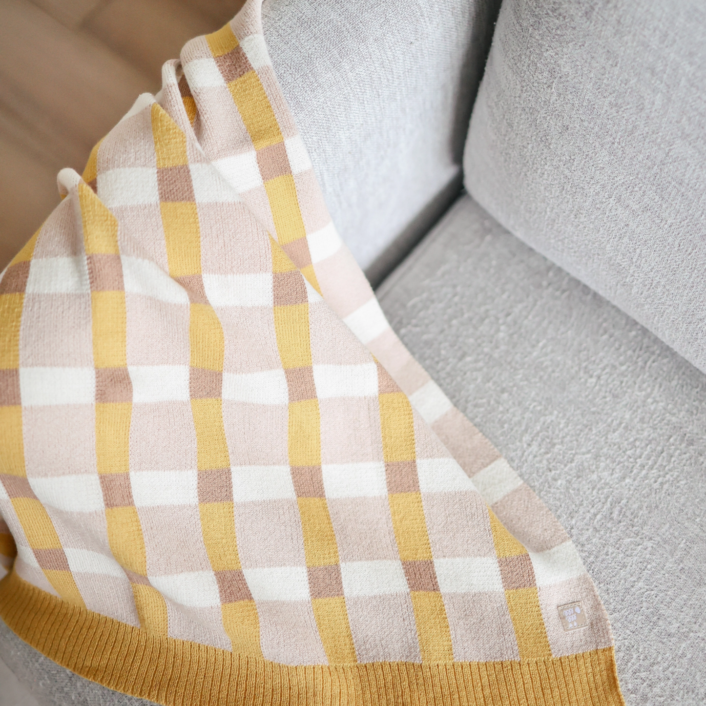 Plaid-patterned fabric with yellow, beige, and white colors on a textured surface.