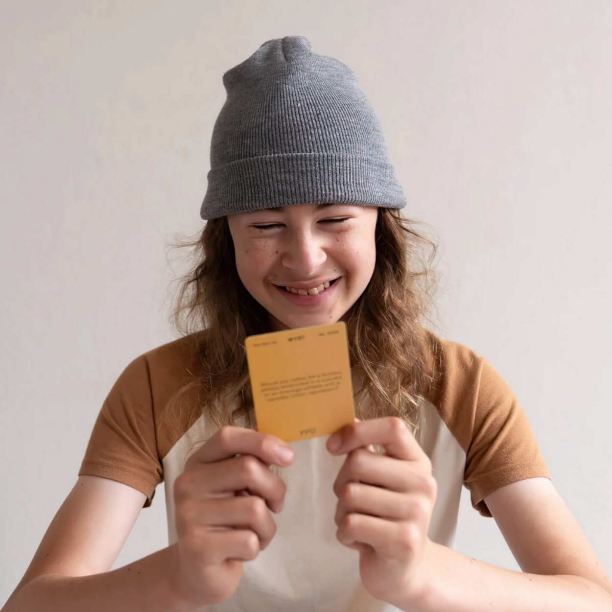 Person wearing a gray beanie holding a yellow card against a plain background