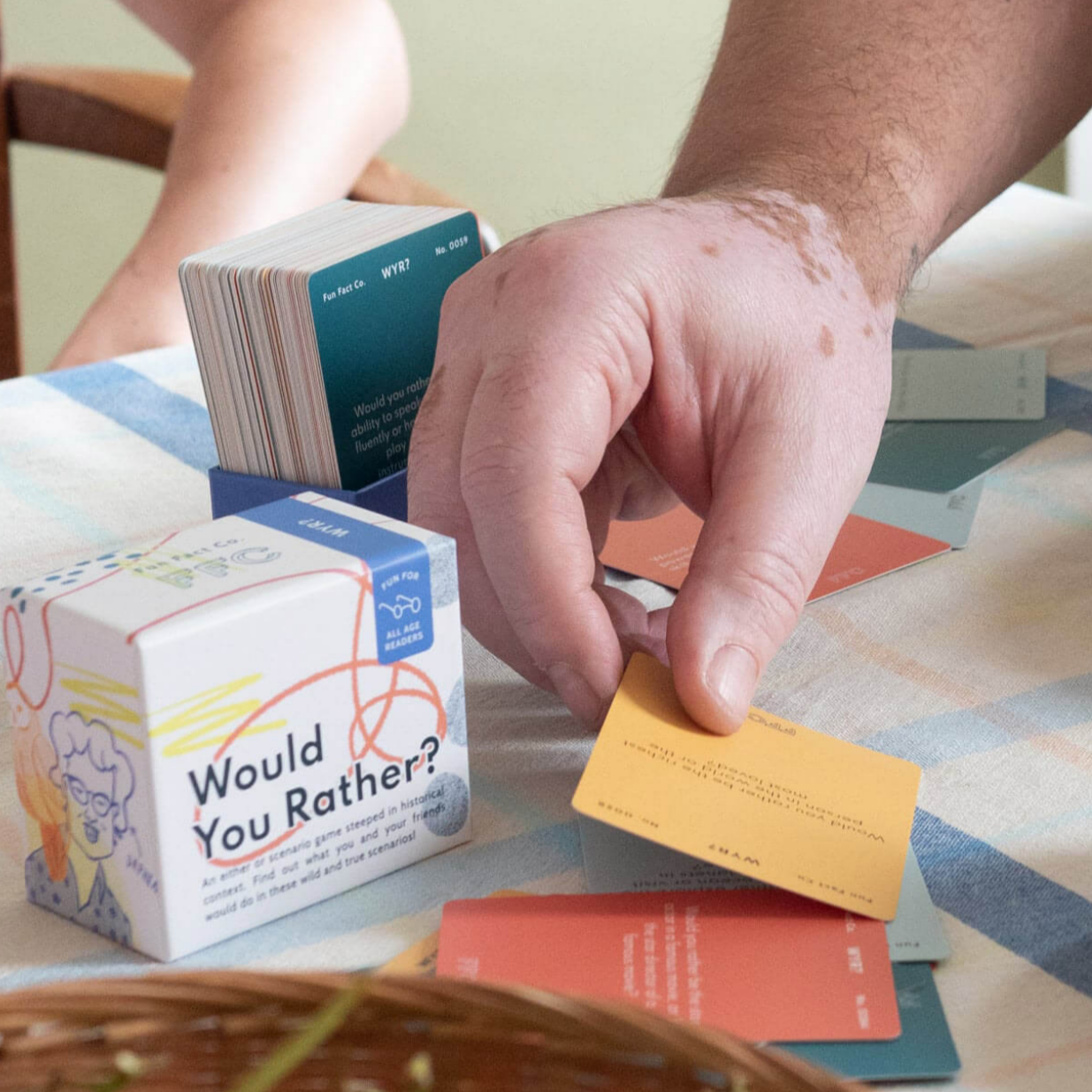 Person playing 'Would You Rather?' card game with colorful cards and box on a table.