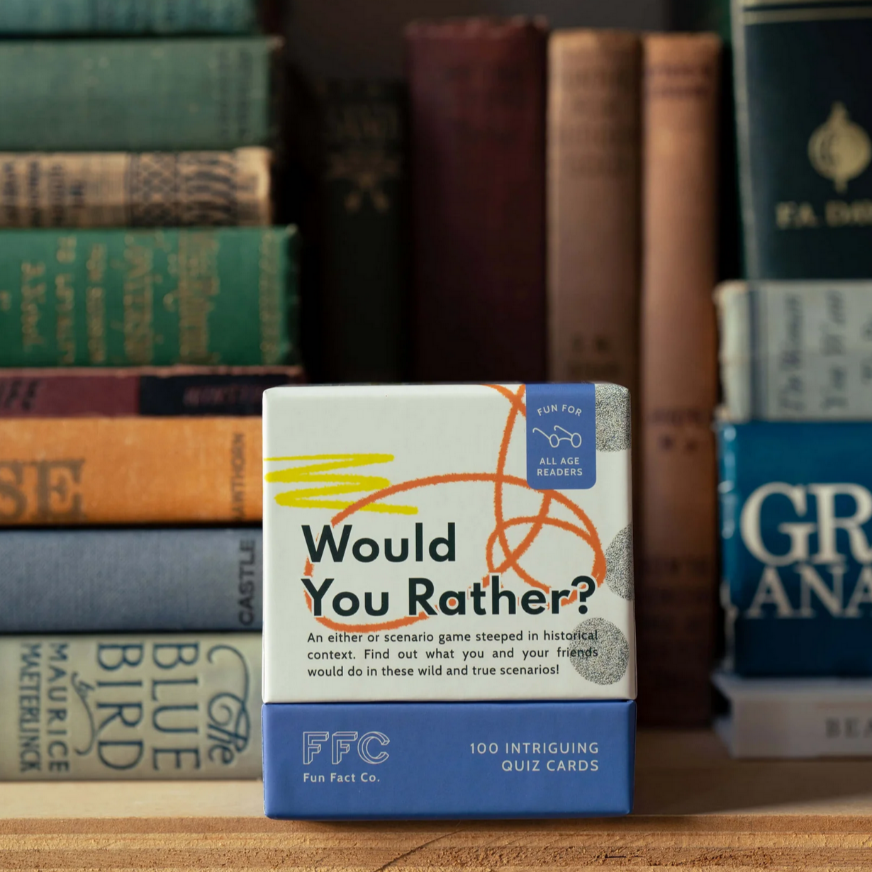 Board game box titled 'Would You Rather?' by FFC on a wooden surface with books in the background