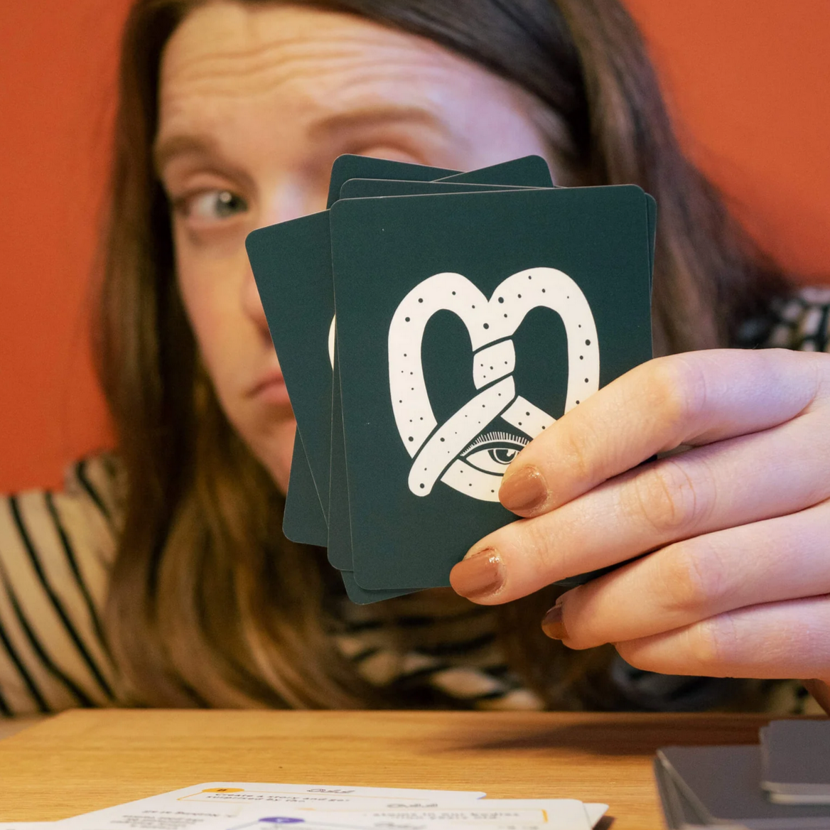 Person holding playing cards with a heart and eye design against an orange wall.