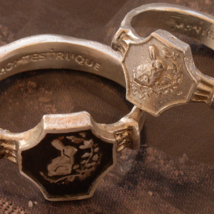 Close-up of two silver rings with intricate designs on a textured surface