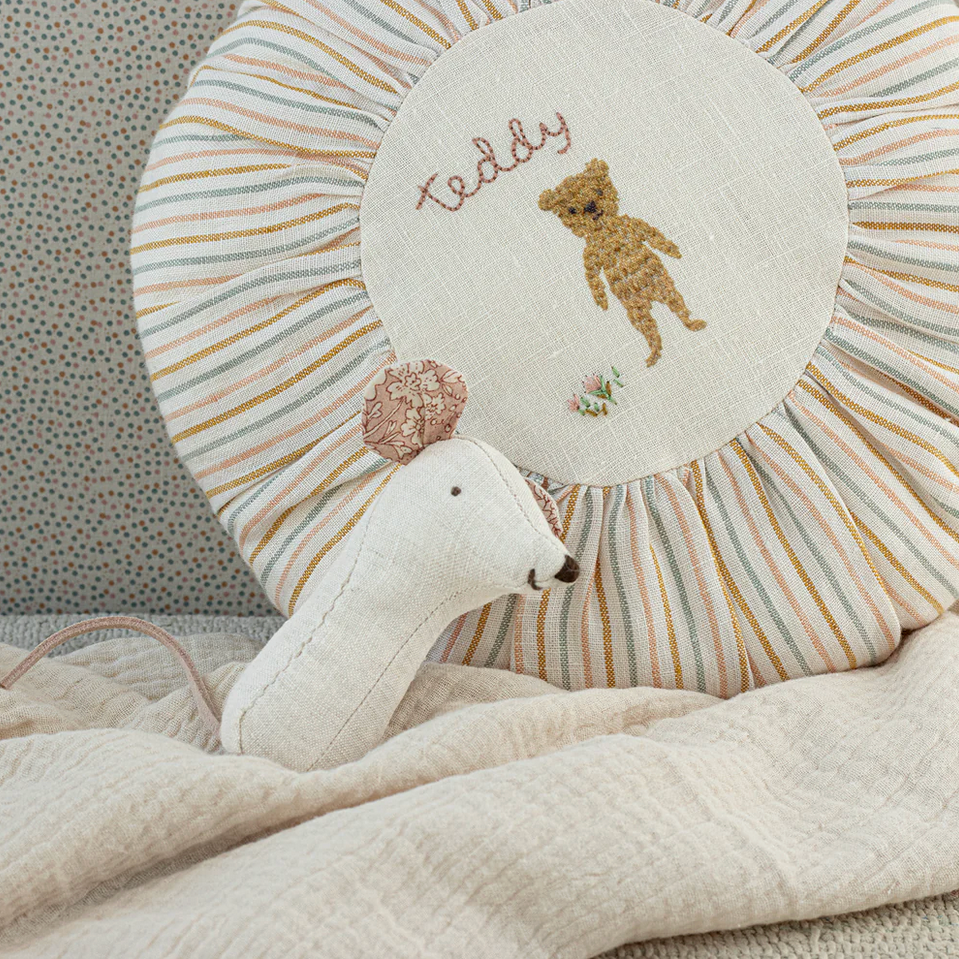 Decorative pillow with teddy bear design and a stuffed animal on a textured surface.