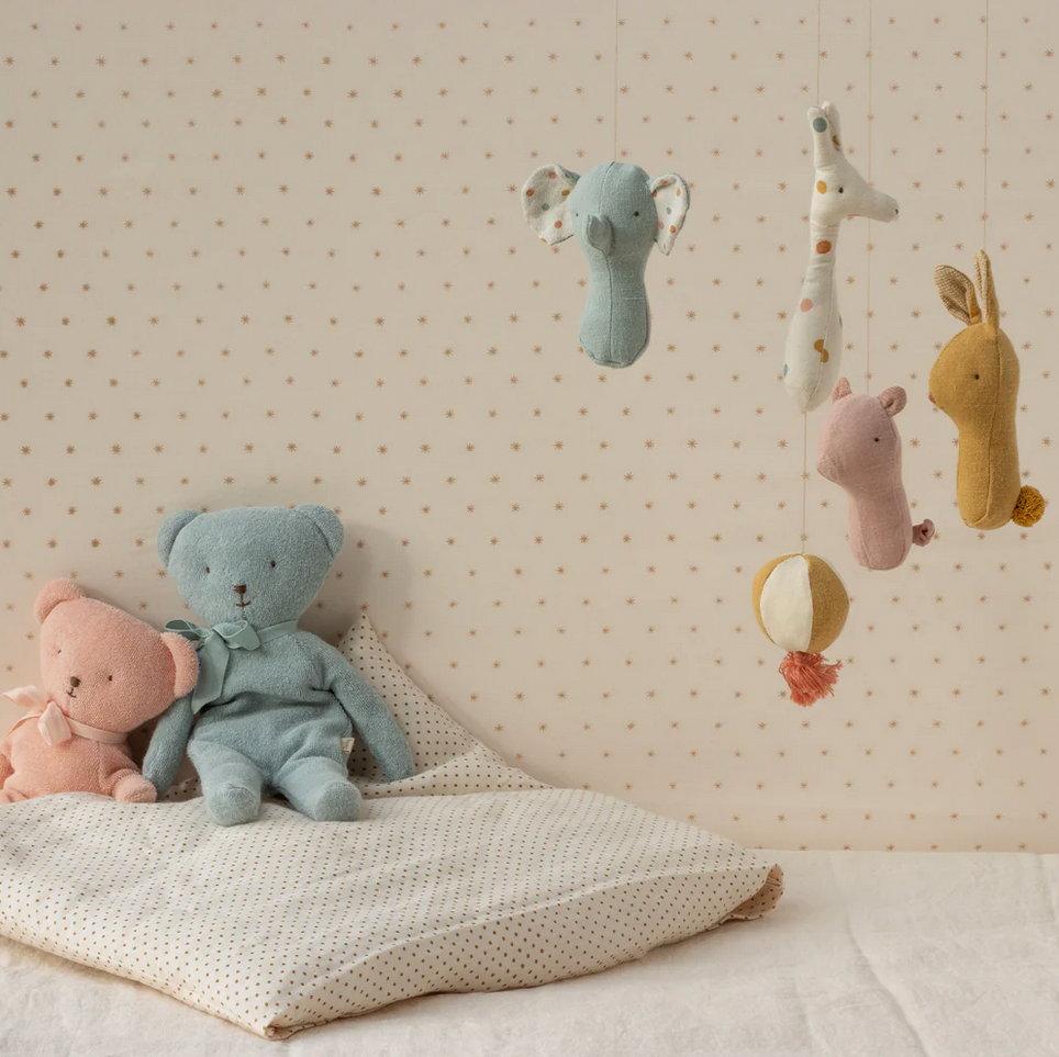 Children's toys including a teddy bear and plush animals on a pillow against a polka dot wall.
