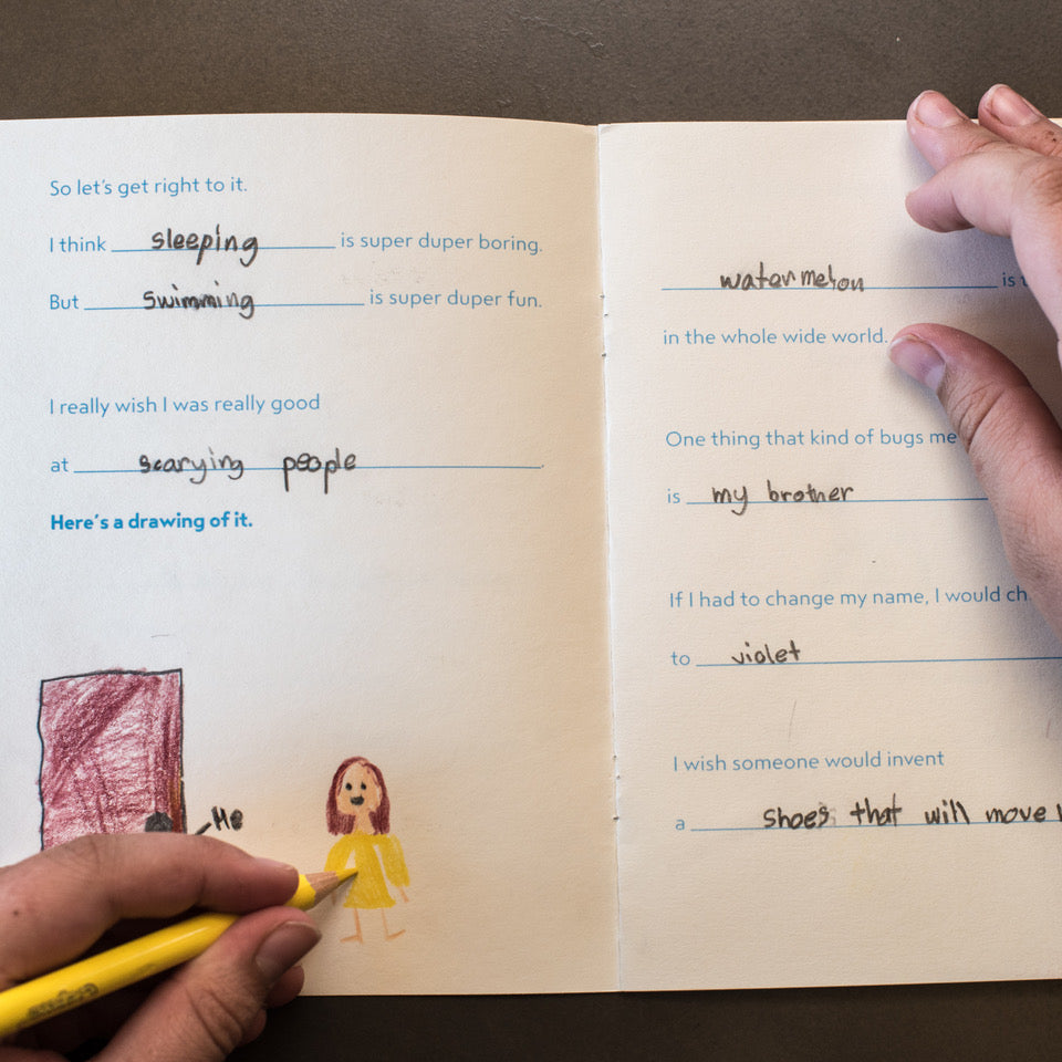 Open book with handwritten text and drawings, held by a person.