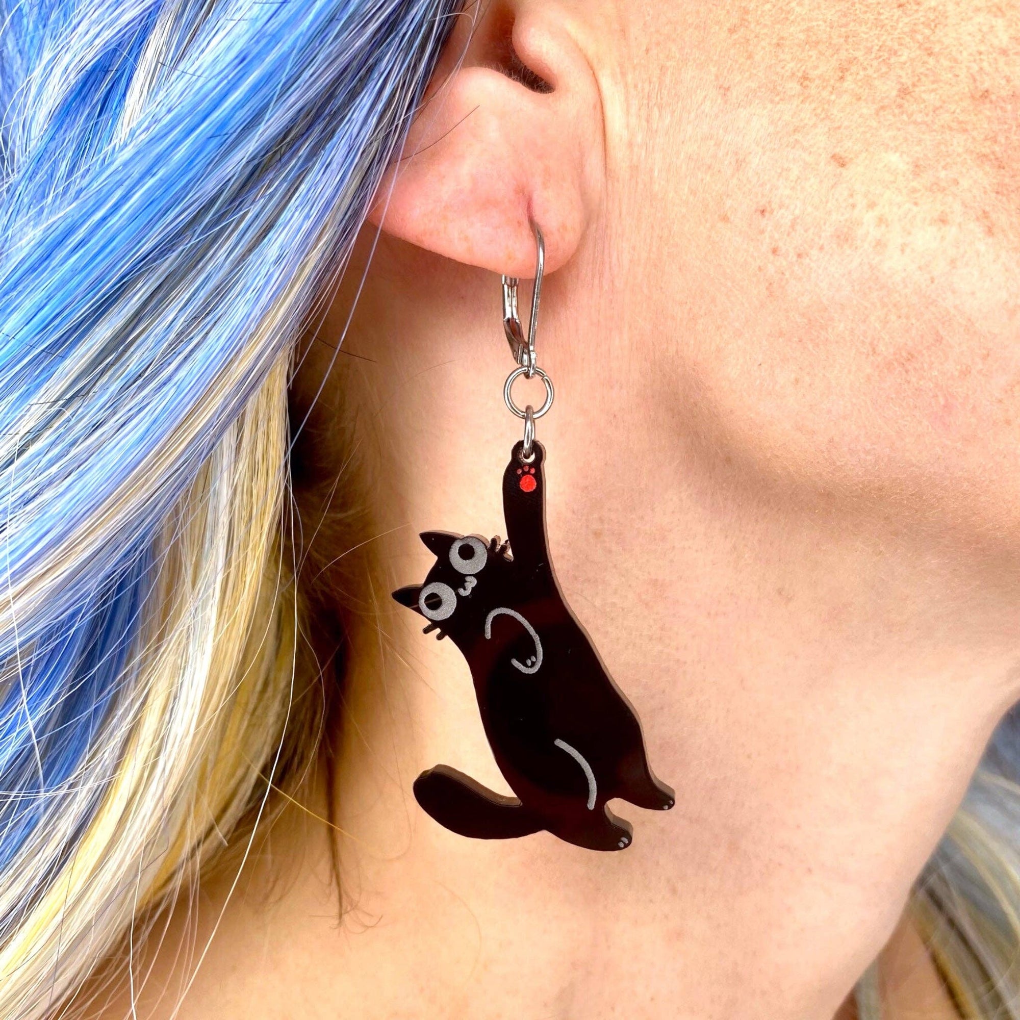 Person wearing a black cat-shaped earring with a red heart on an ear.