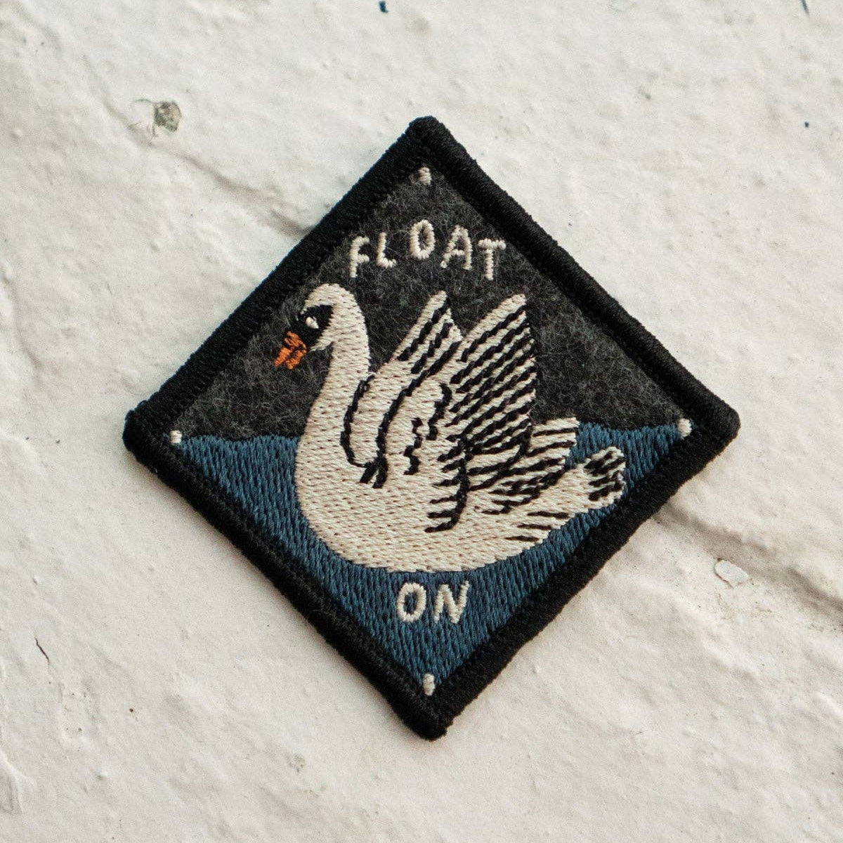 Embroidered patch with a swan design and 'FLOAT ON' text on a textured white background