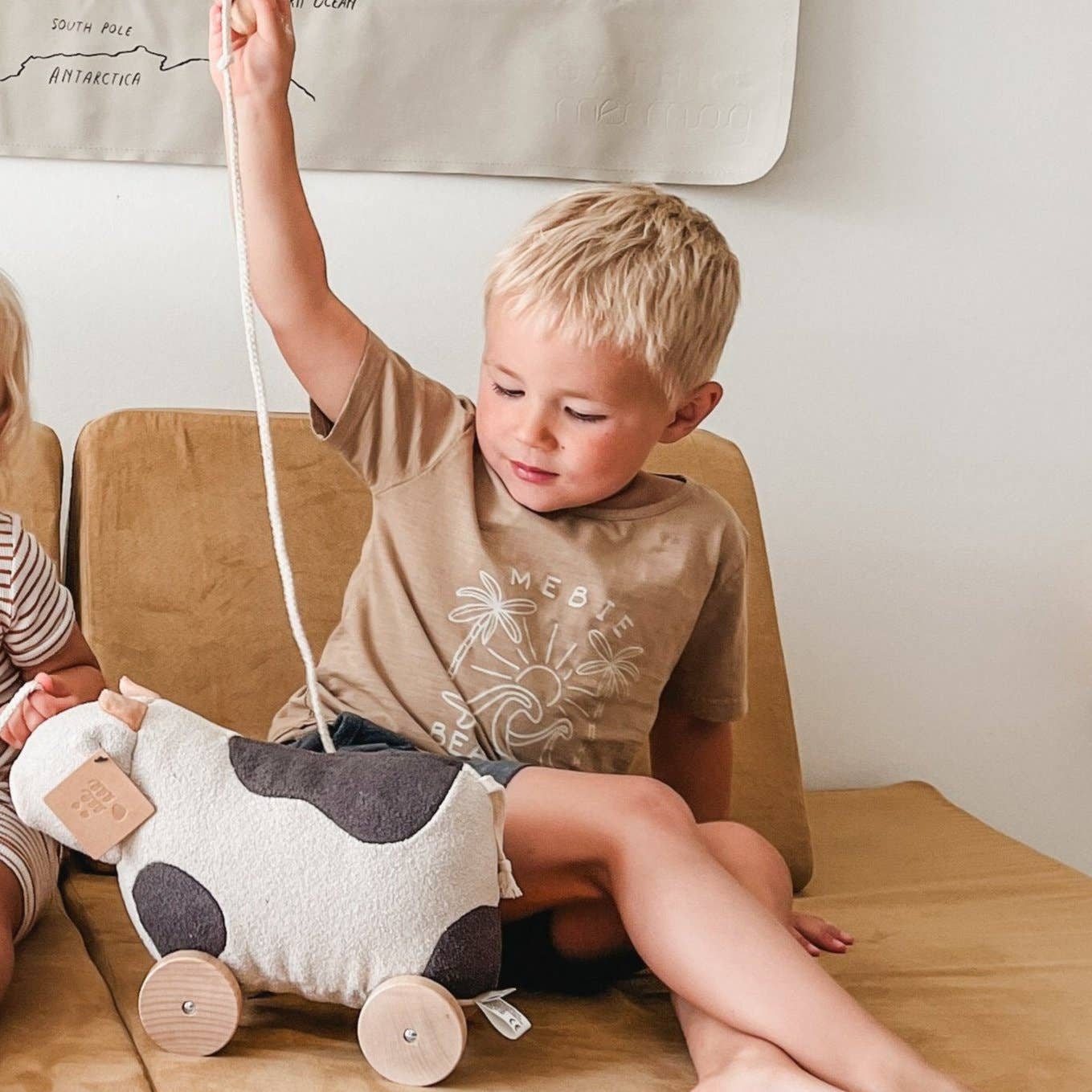 Child playing with a cow-shaped toy on a wooden floor.