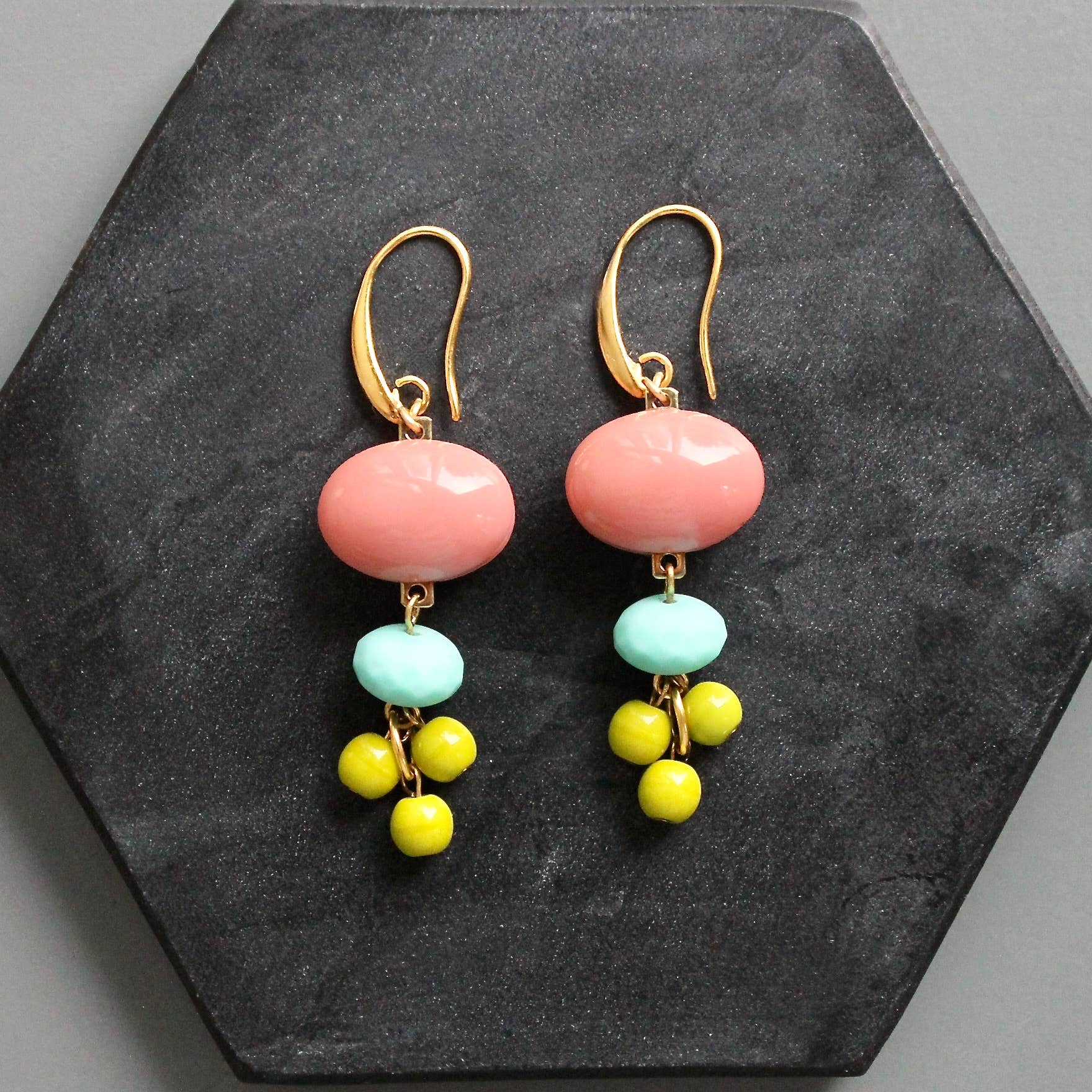 Pair of earrings with pink, turquoise, and yellow beads on a dark stone surface