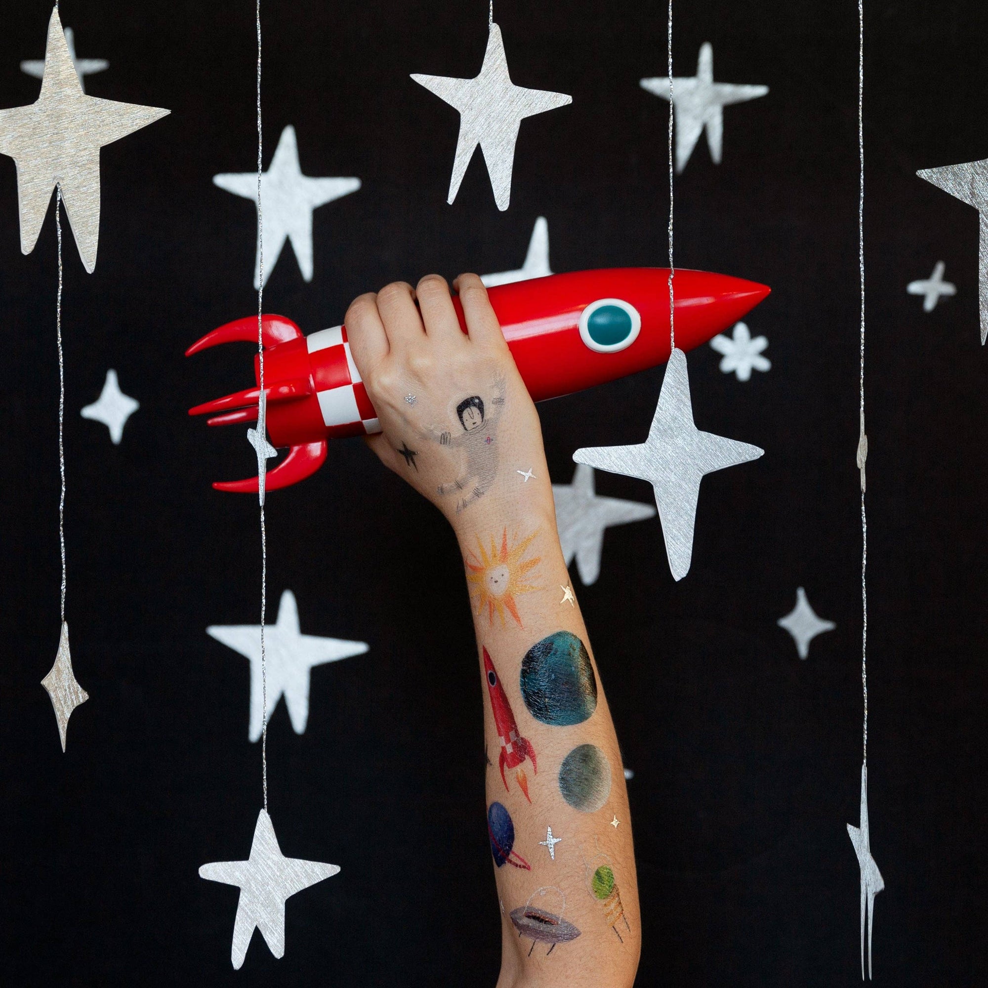 Hand holding a red toy rocket against a black background with white stars
