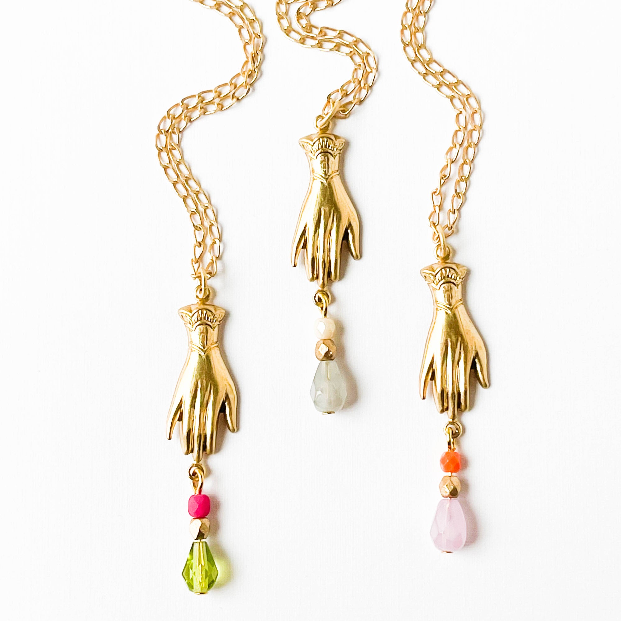Gold hand-shaped pendants with colorful beads on a white background