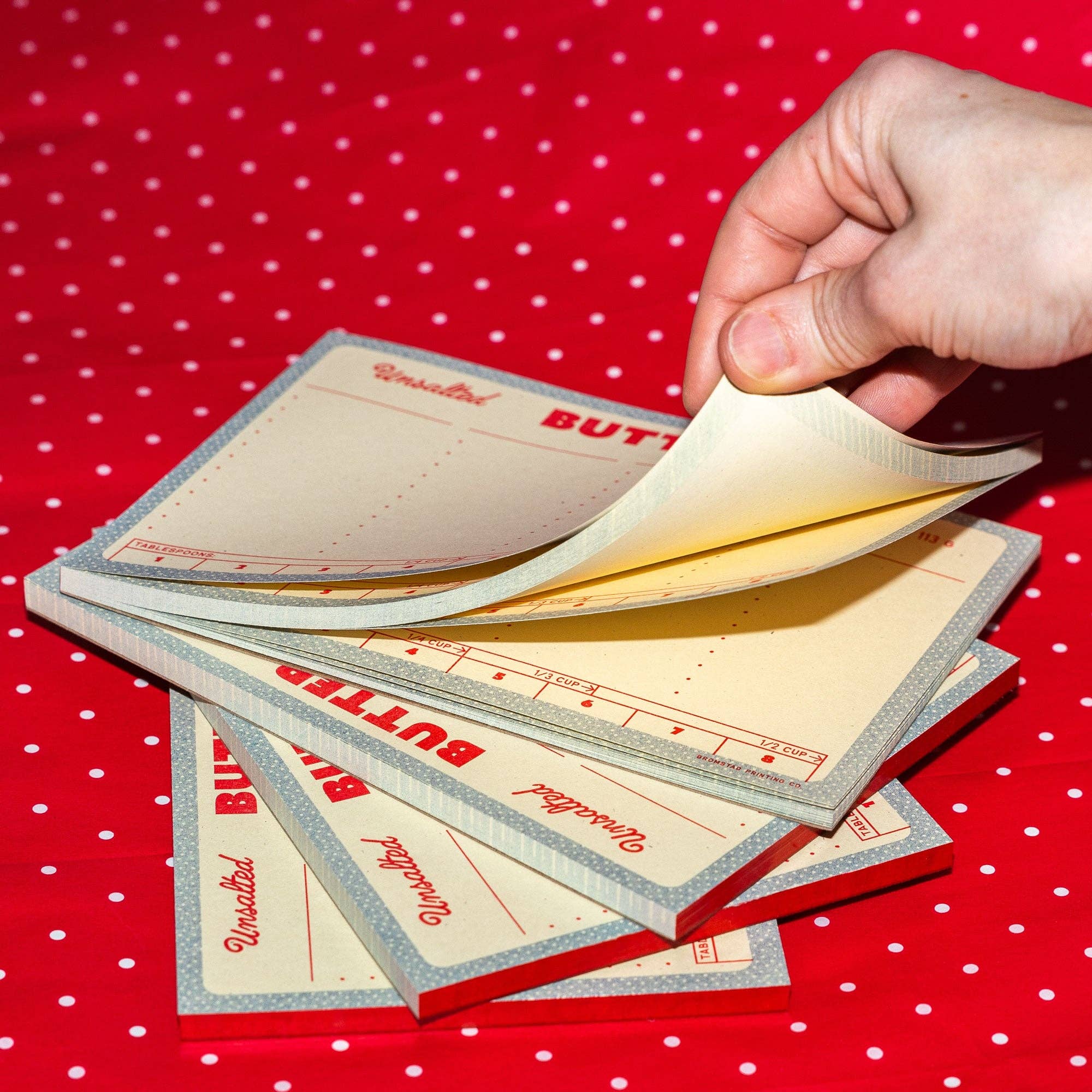 Hand holding a stack of butter packaging sheets against a red polka dot background