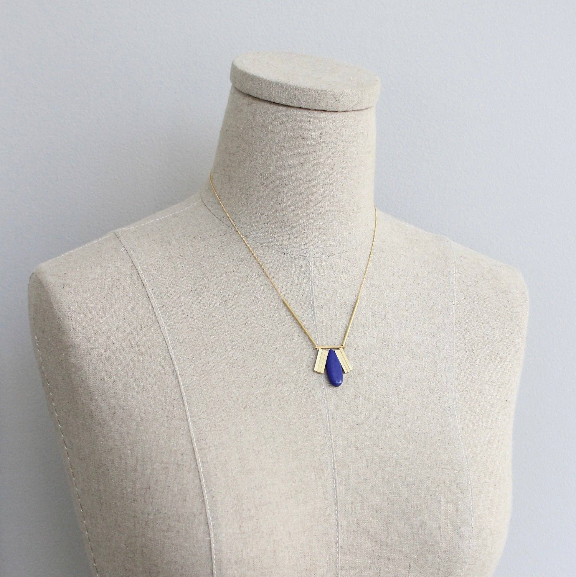 Necklace with a blue pendant on a mannequin against a plain background