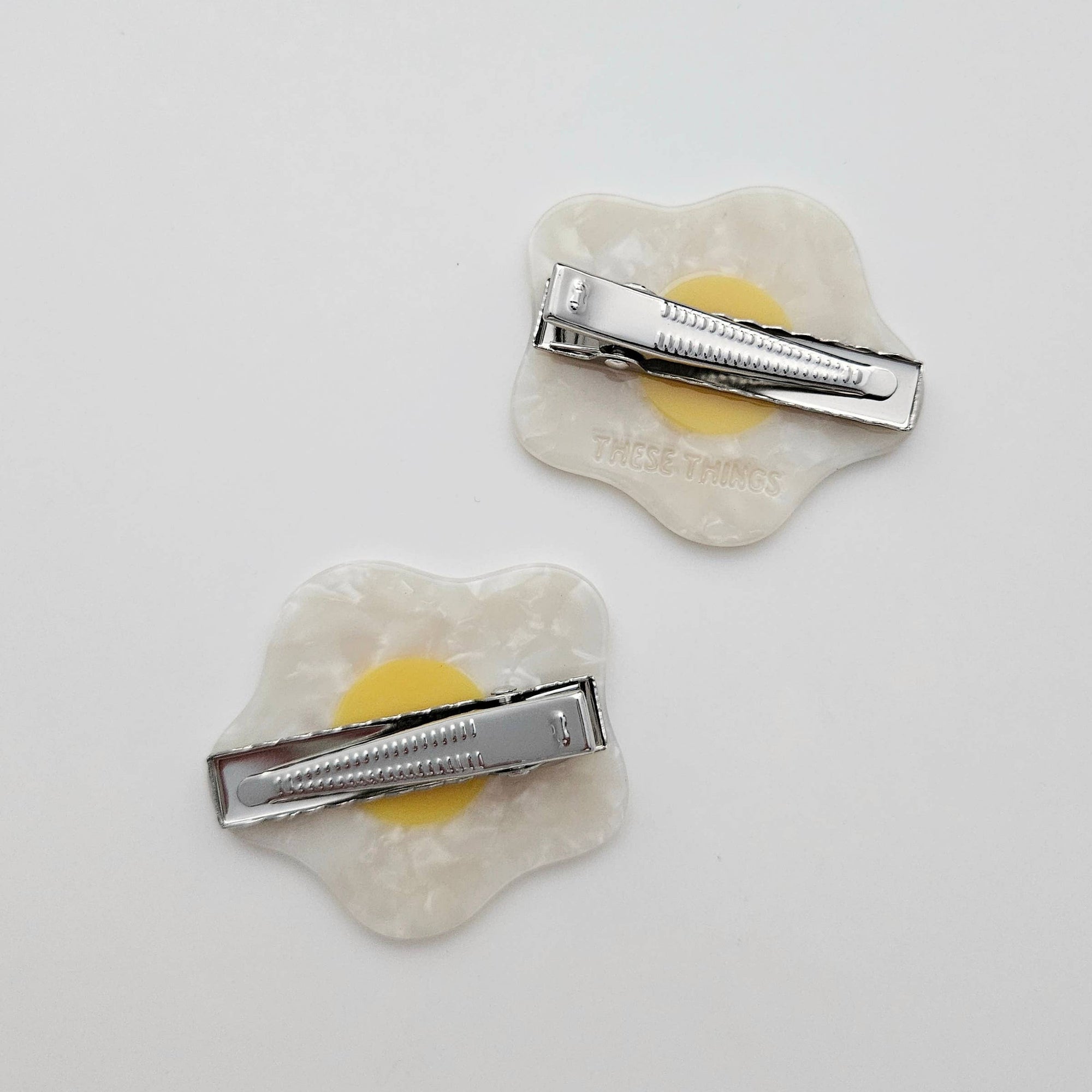Two egg-shaped hair clips with a silver barrette on a light gray background