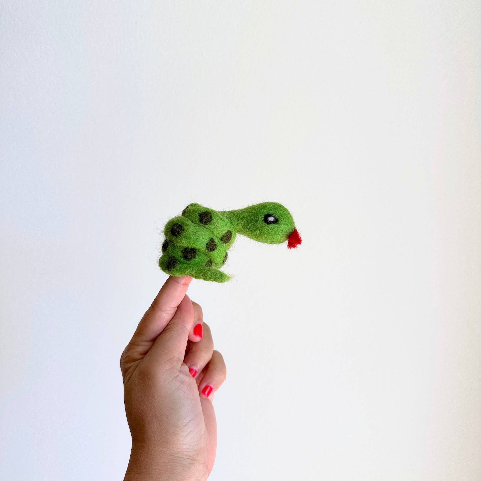 Hand holding a small green snake plush toy against a white background