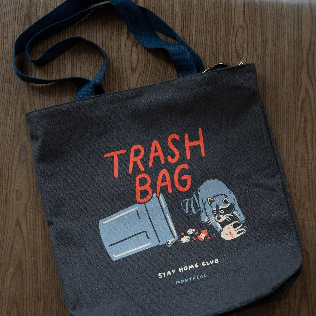 Black tote bag with 'Trash Bag' text and graphic on a wooden surface