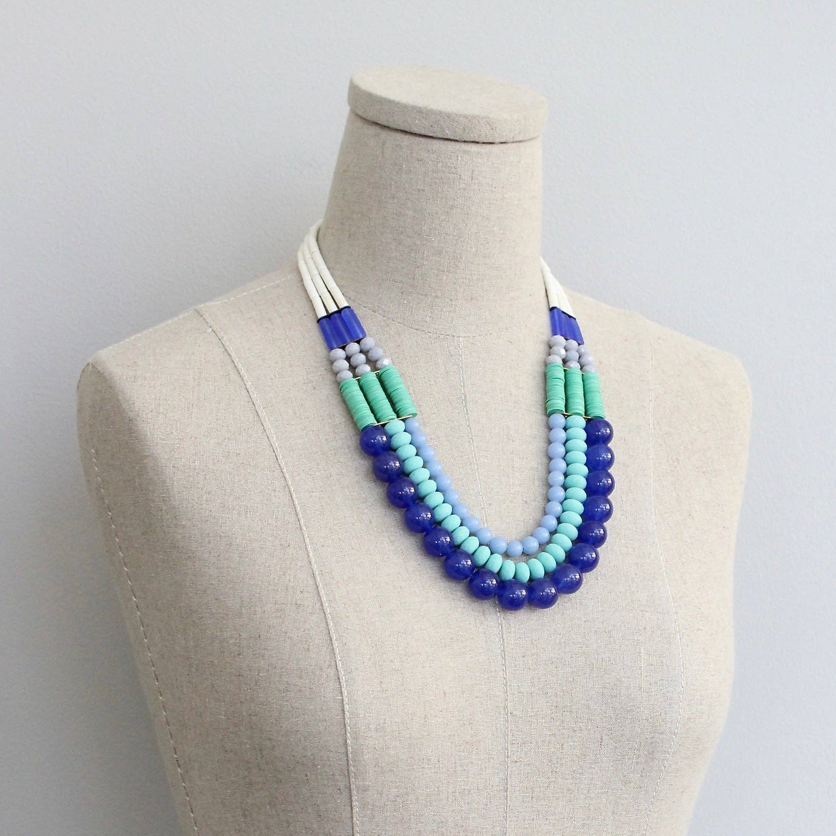 Necklace with blue and green beads on a mannequin against a plain background