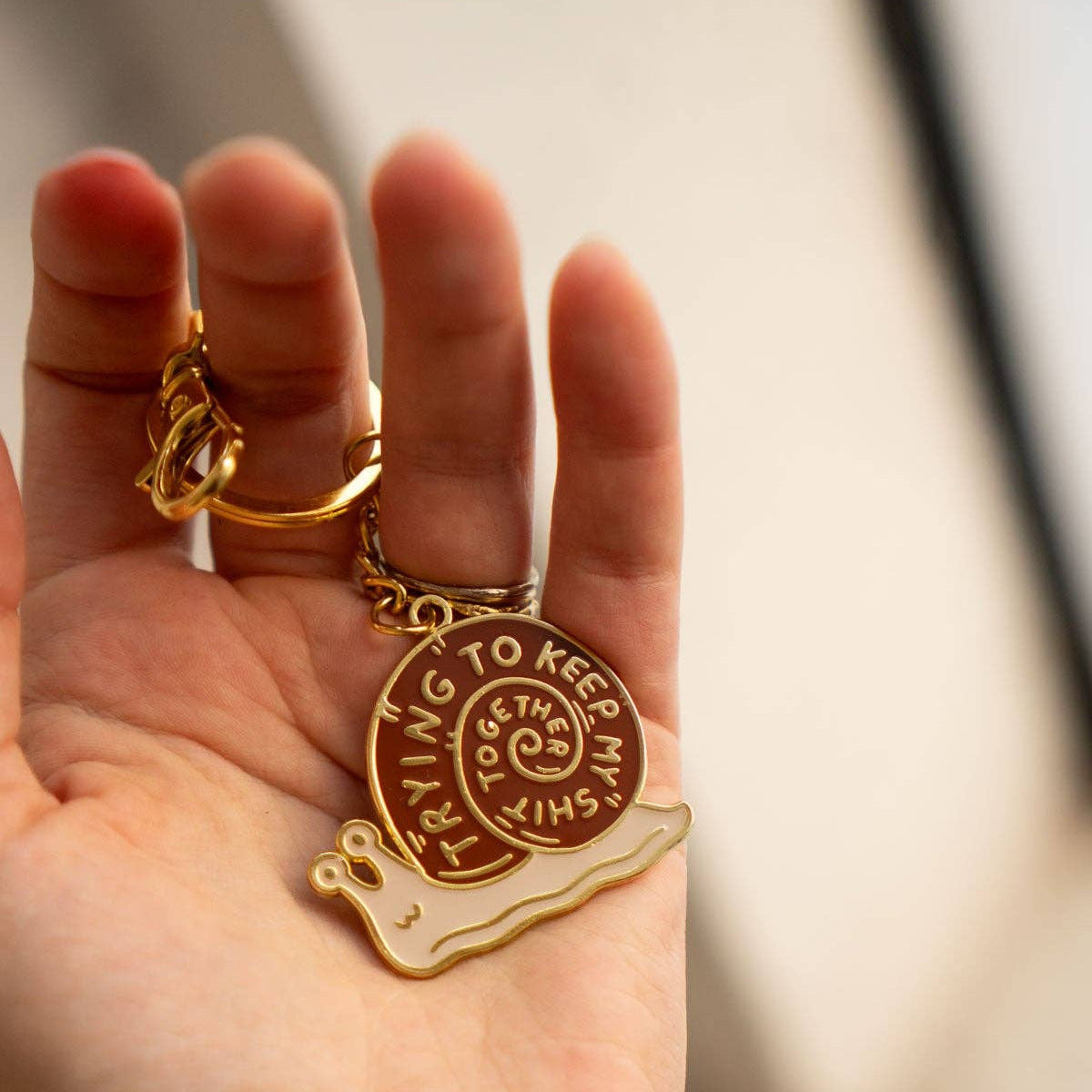 Gold KEYchain with a pendant held in a hand against a neutral background