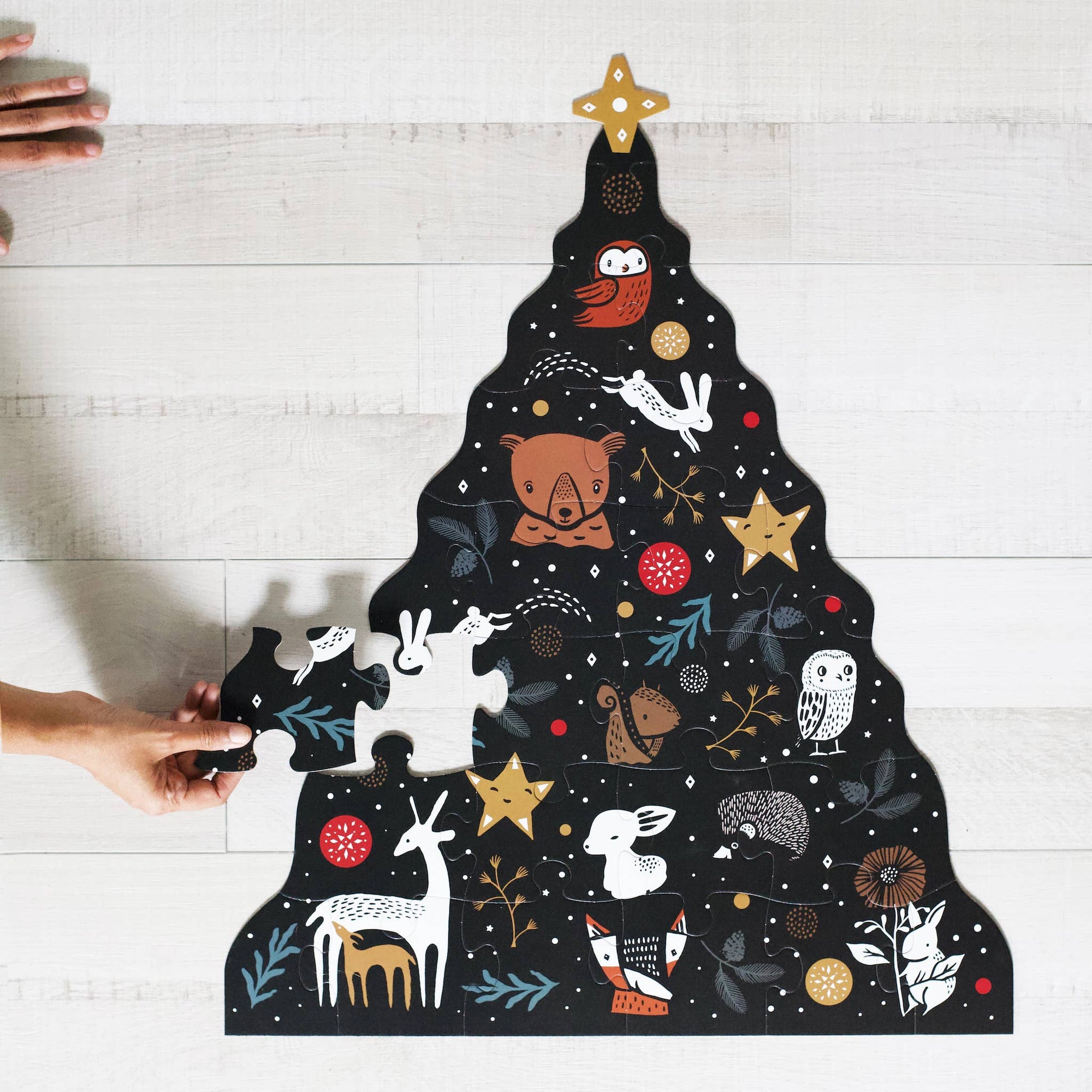A puzzle piece with a Christmas tree design, featuring animal illustrations and a star at the top. The piece is black with white and gold accents.