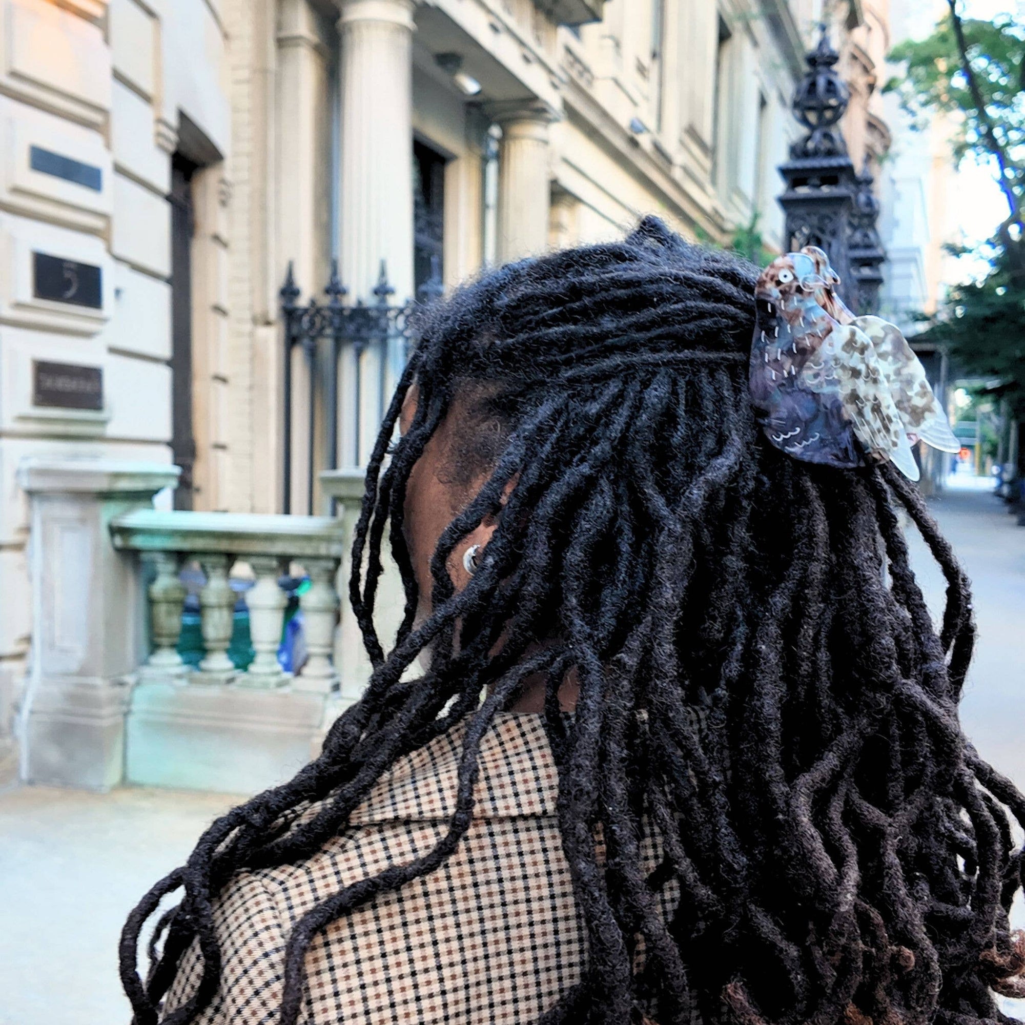 Person with long braided hair wearing a plaid coat in an urban setting