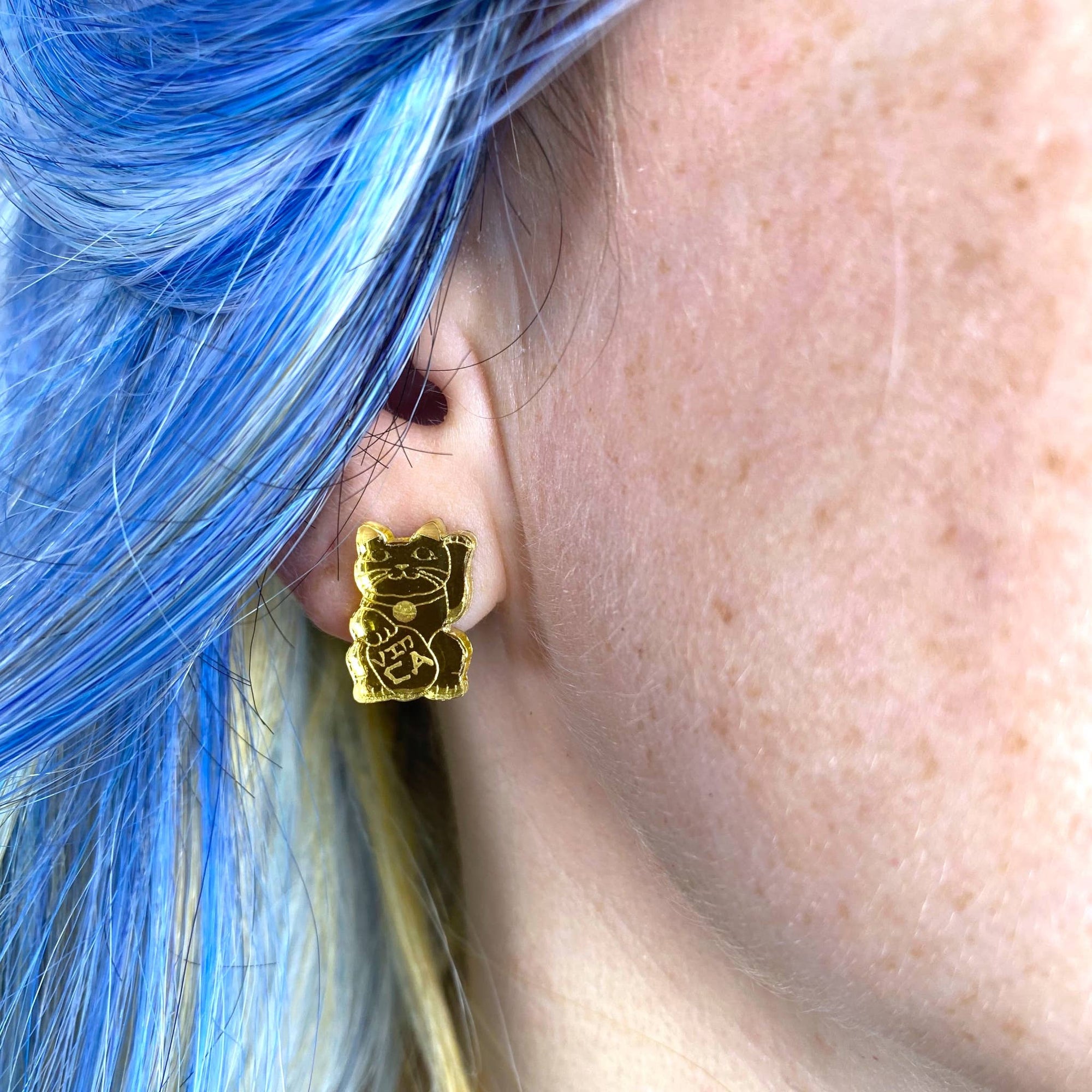 Gold cat-shaped earring worn by a person with blue hair.