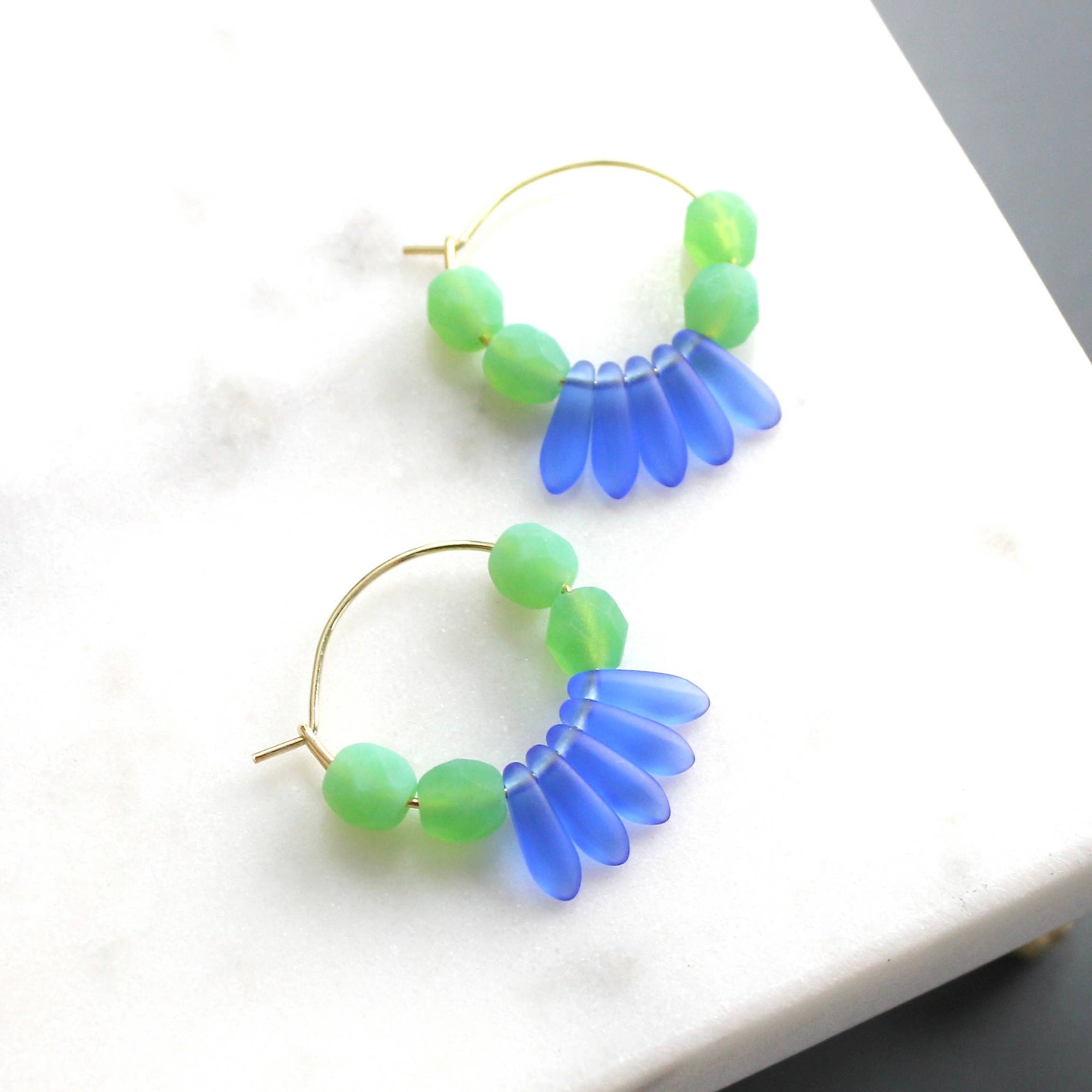 Pair of hoop earrings with green and blue beaded design on a white surface.