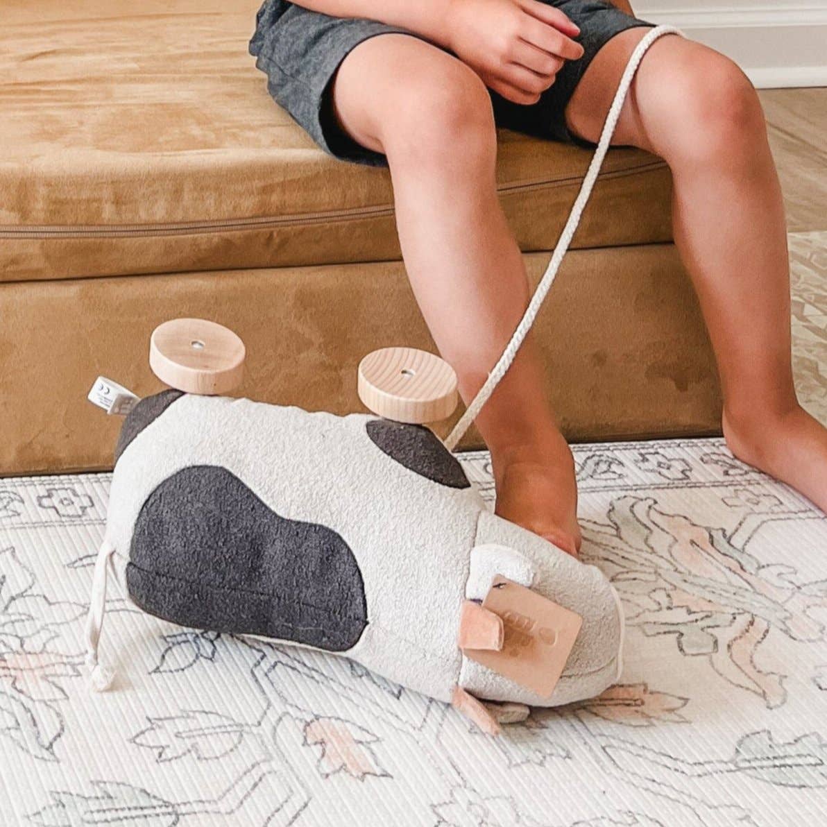 Child playing with a cow-shaped toy on a patterned rug