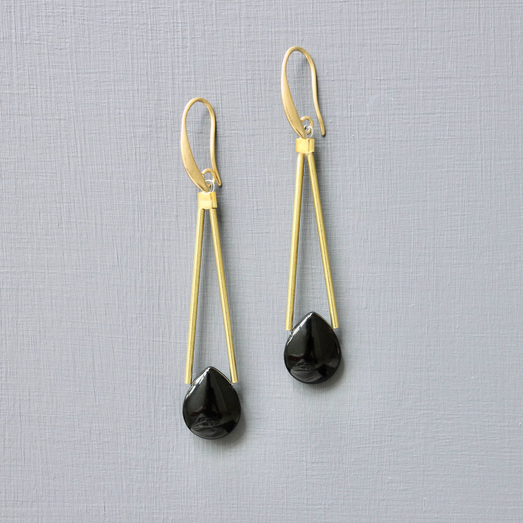 Gold earrings with black teardrop-shaped drops on a gray background
