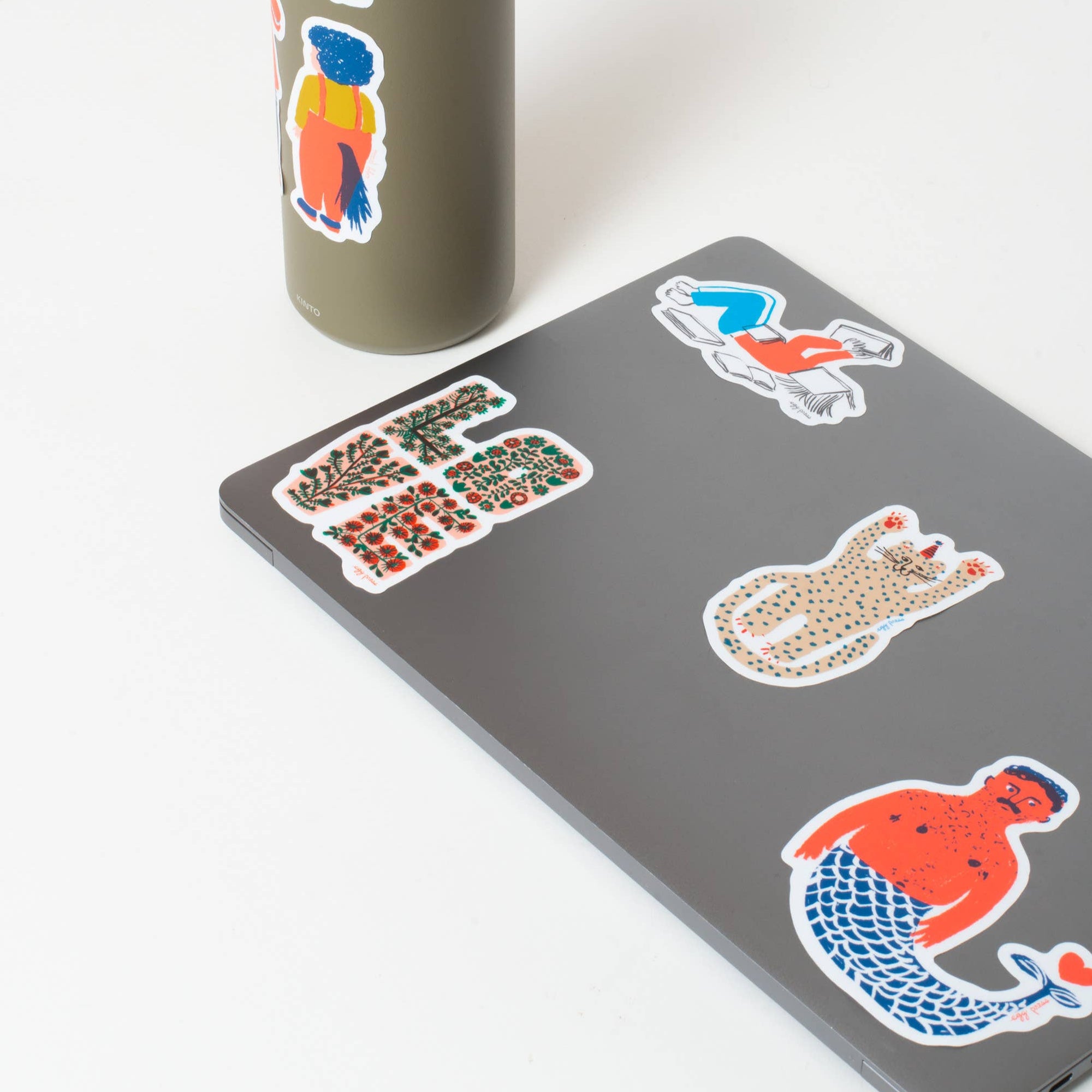Gray tumbler and computer with colorful stickers on a white background