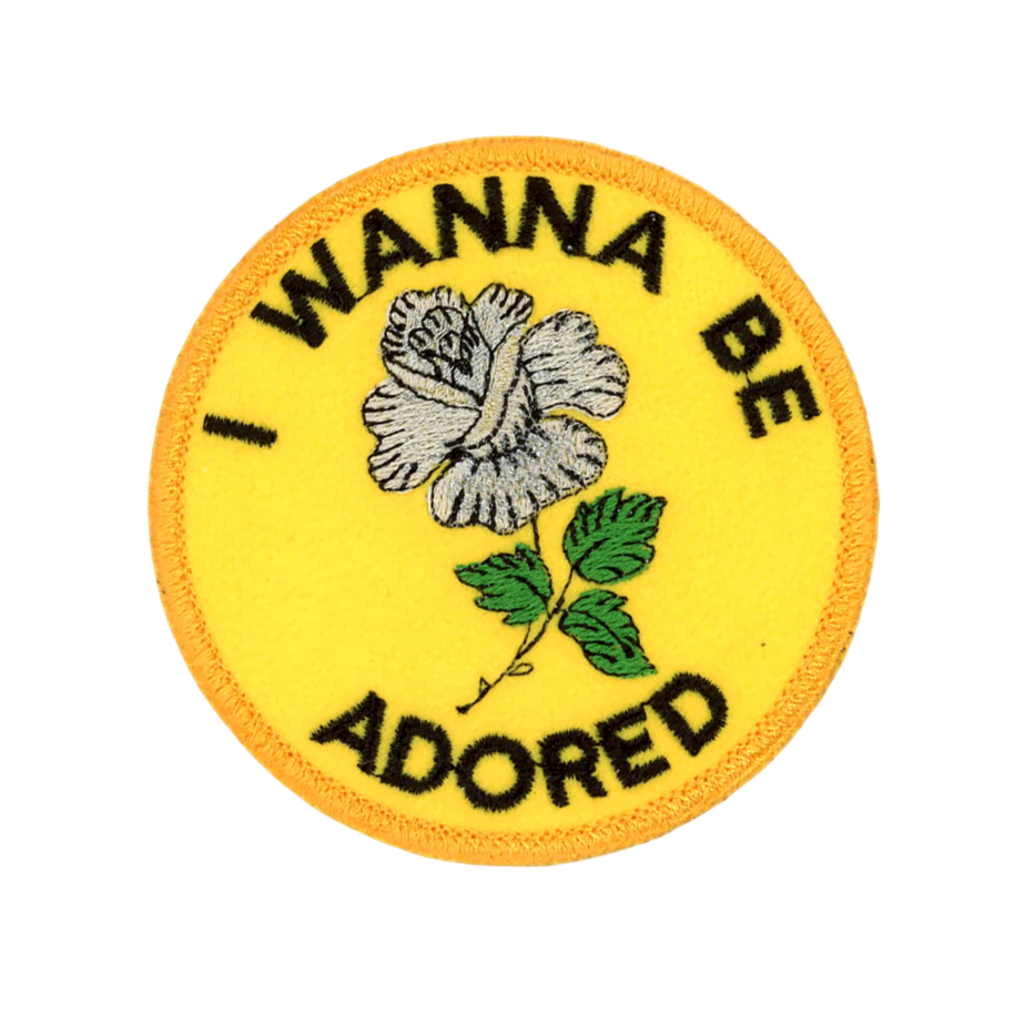 Circular patch with a flower design and text 'I Wanna Be Adored' on a yellow background