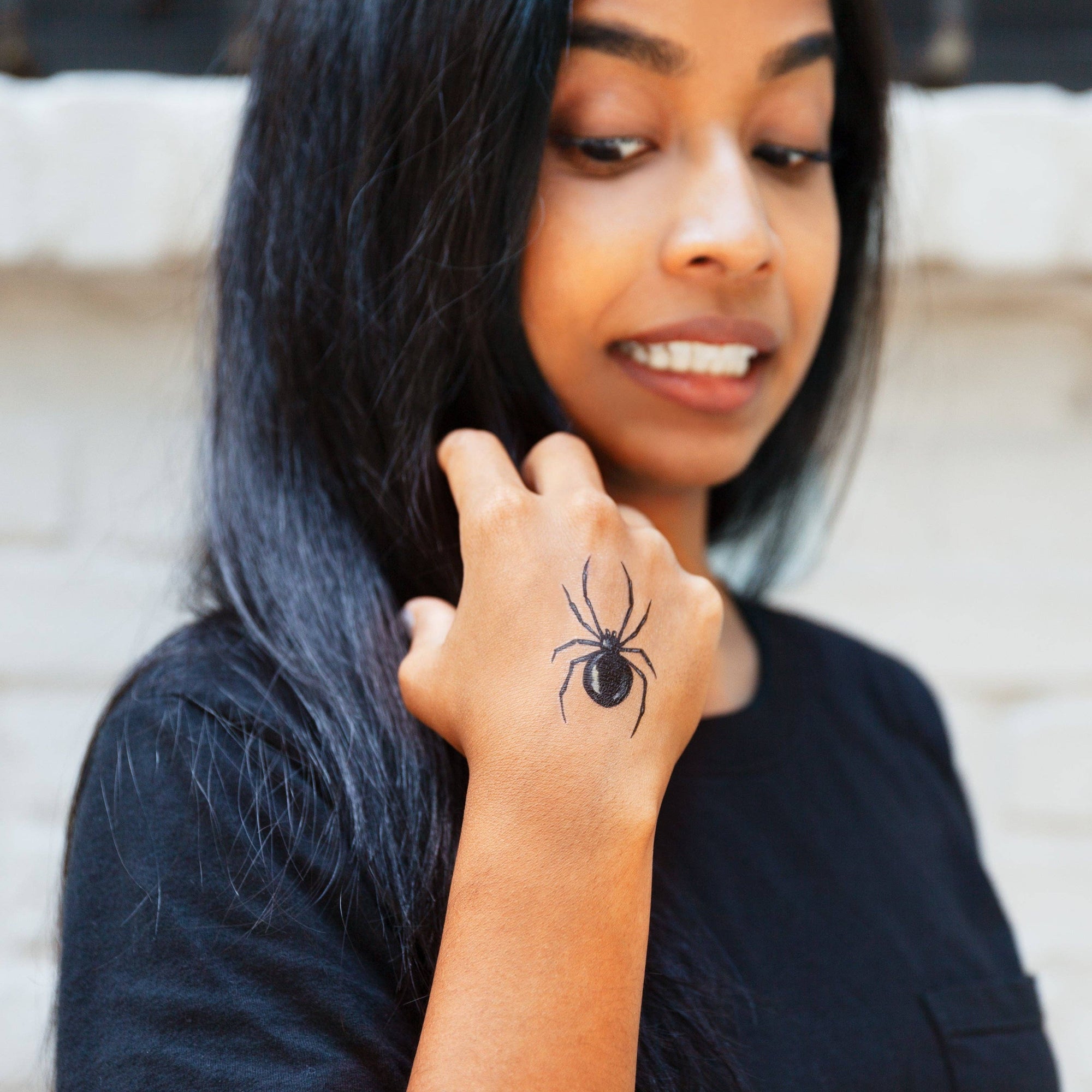 Woman with a spider tattoo on her hand, wearing a black top.