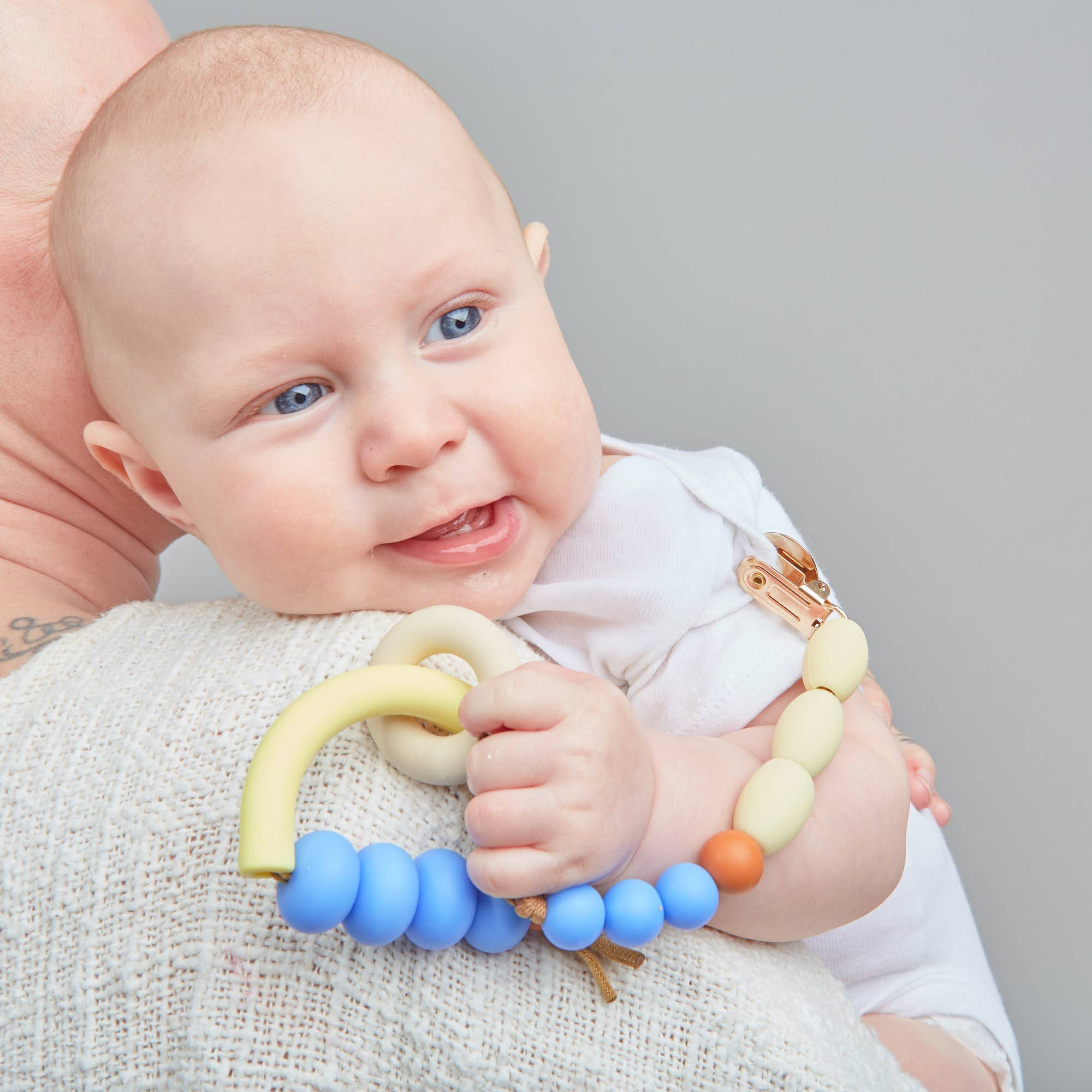 Baby holding a colorful teething ring with a neutral background