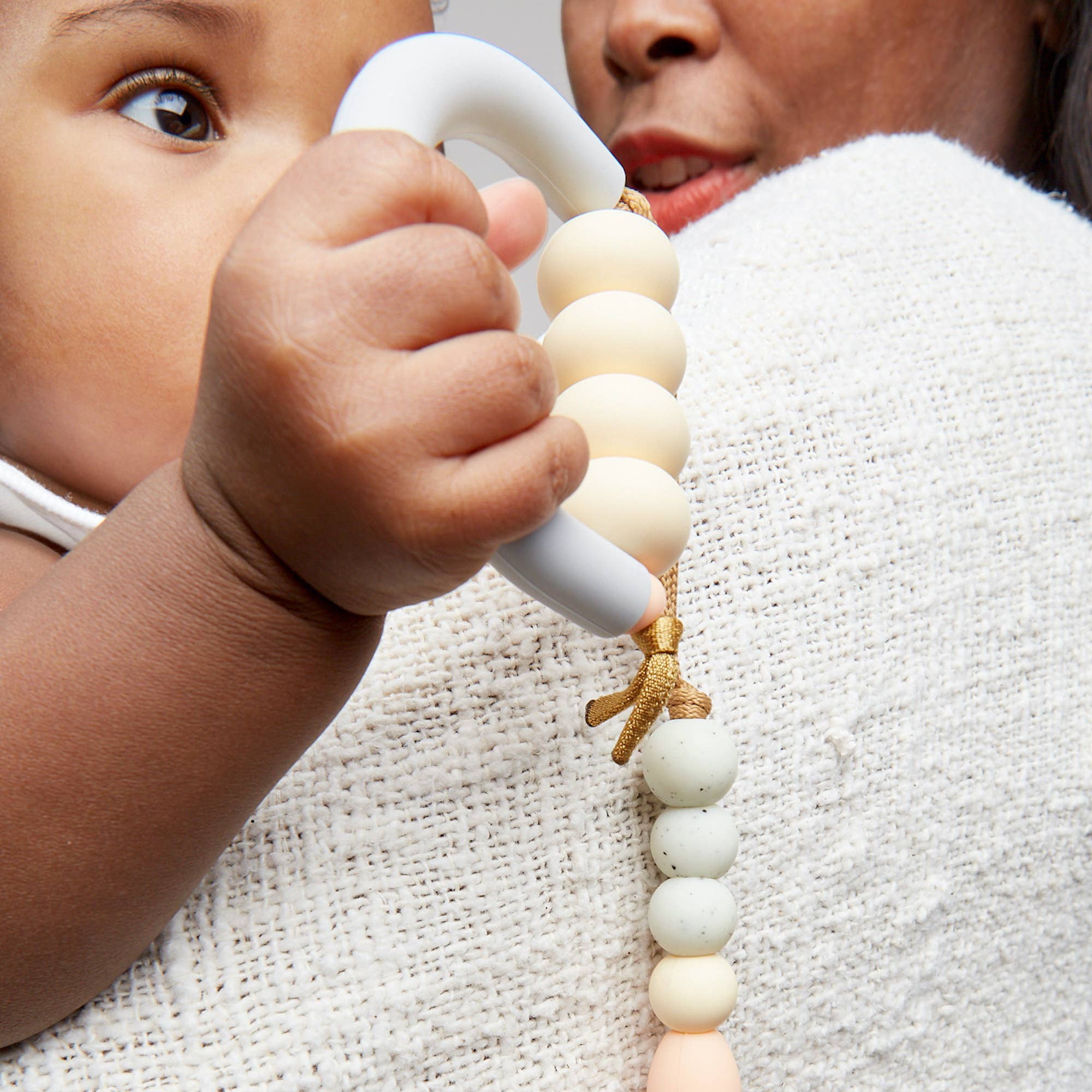 Close-up of a baby holding a teething ring with wooden beads.