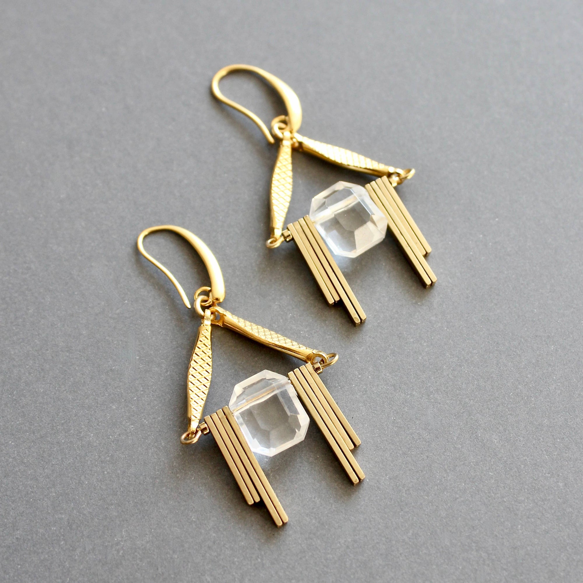 Gold earrings with clear gemstones on a gray background