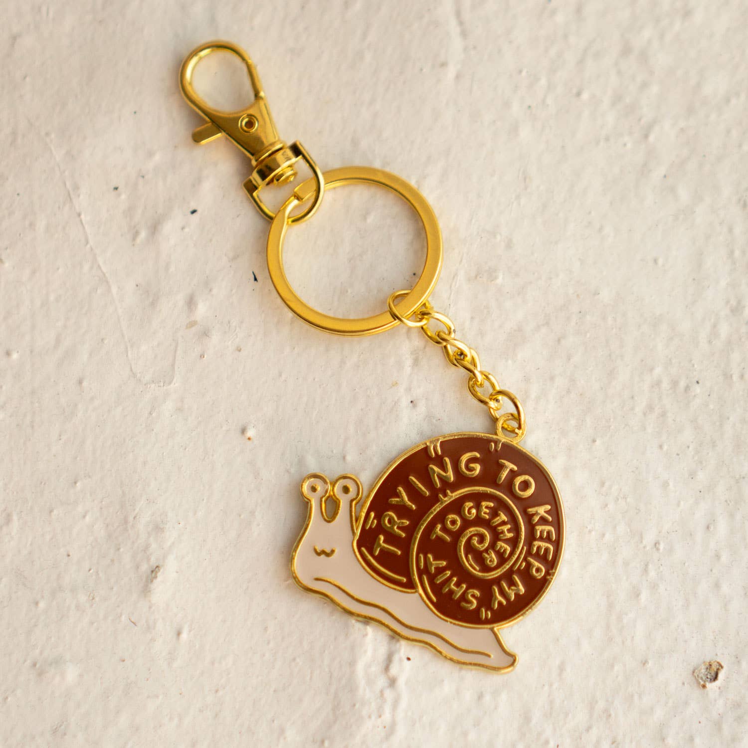Gold and brown snail-shaped keychain on a textured beige background