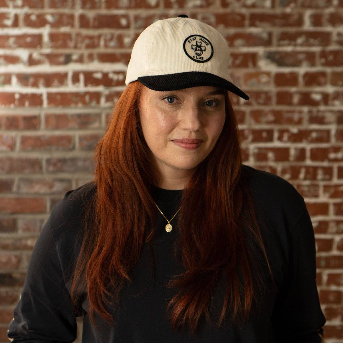 Person wearing a white cap with a black logo against a brick wall