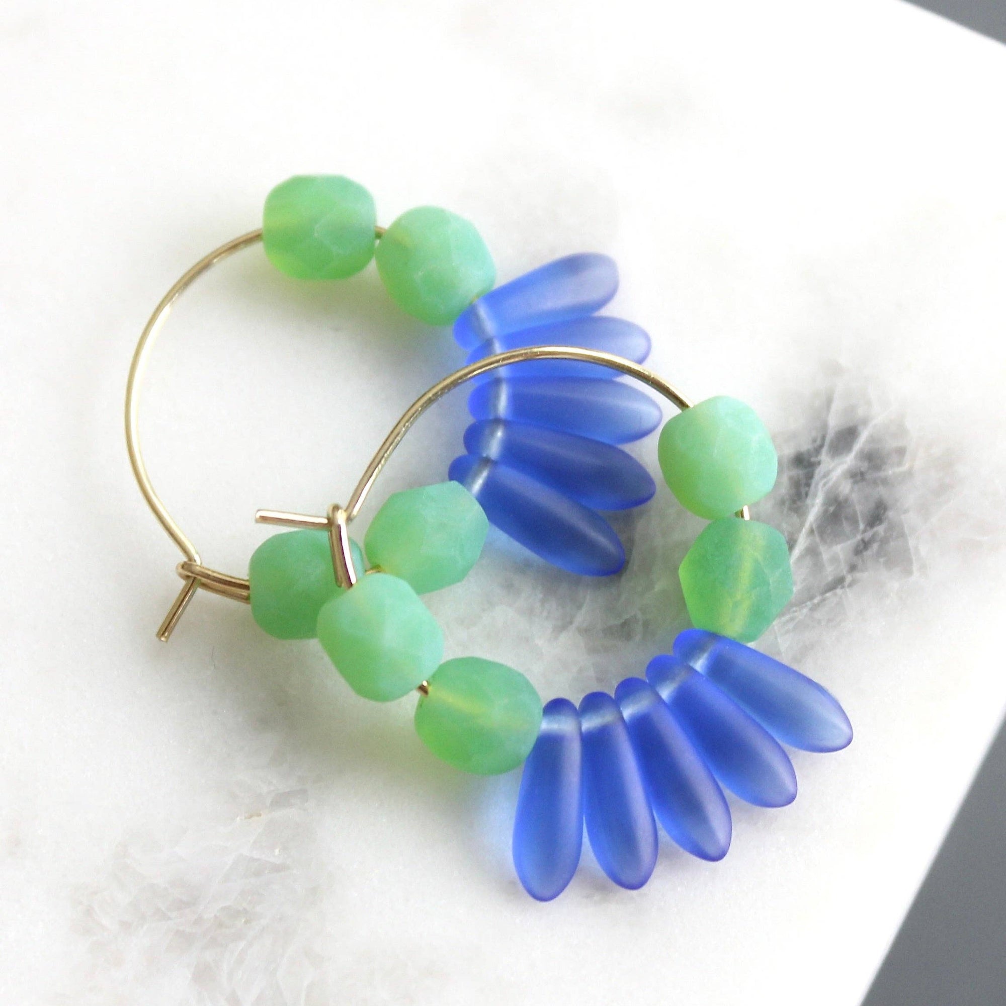 Hoop earrings with blue and green floral beads on a marble surface