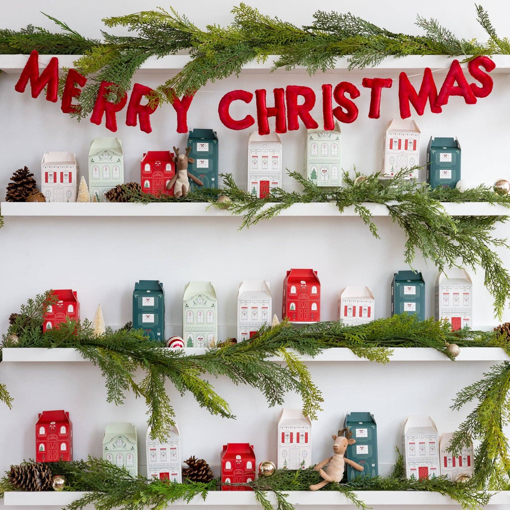 Decorative Christmas shelf with 'Merry Christmas' sign, greenery, and small houses.
