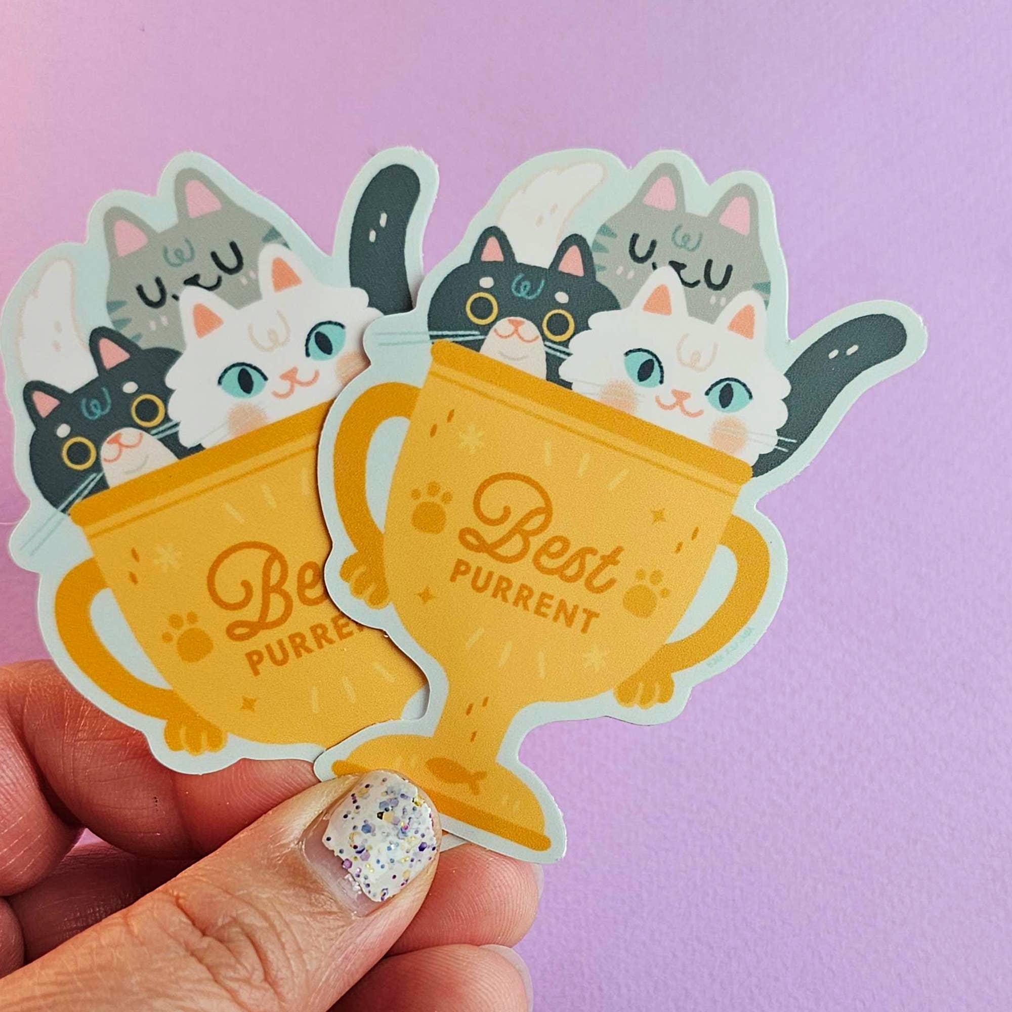 Sticker of a trophy with cats inside, held against a purple background