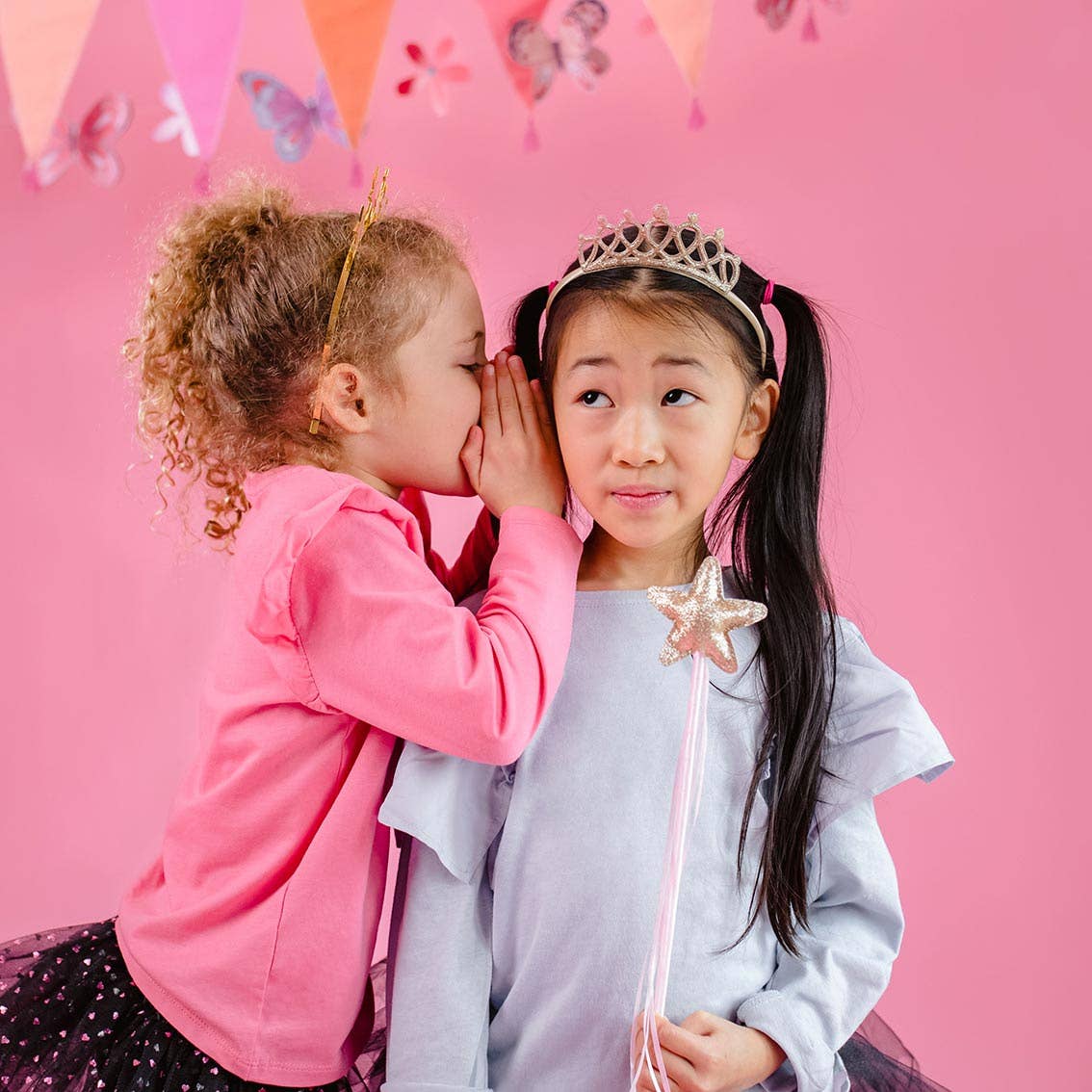 Two children in costumes against a pink background with butterfly decorations