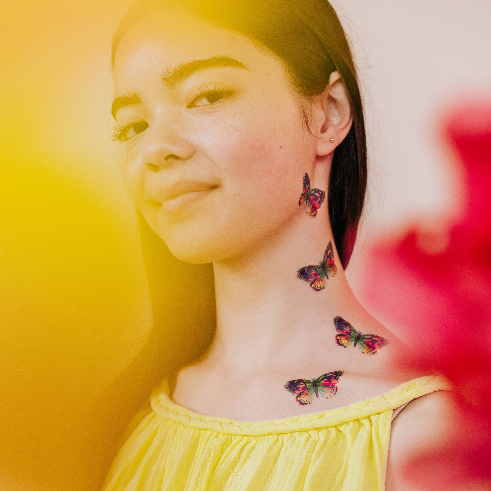 Woman with colorful butterfly tattoos on her neck against a yellow background